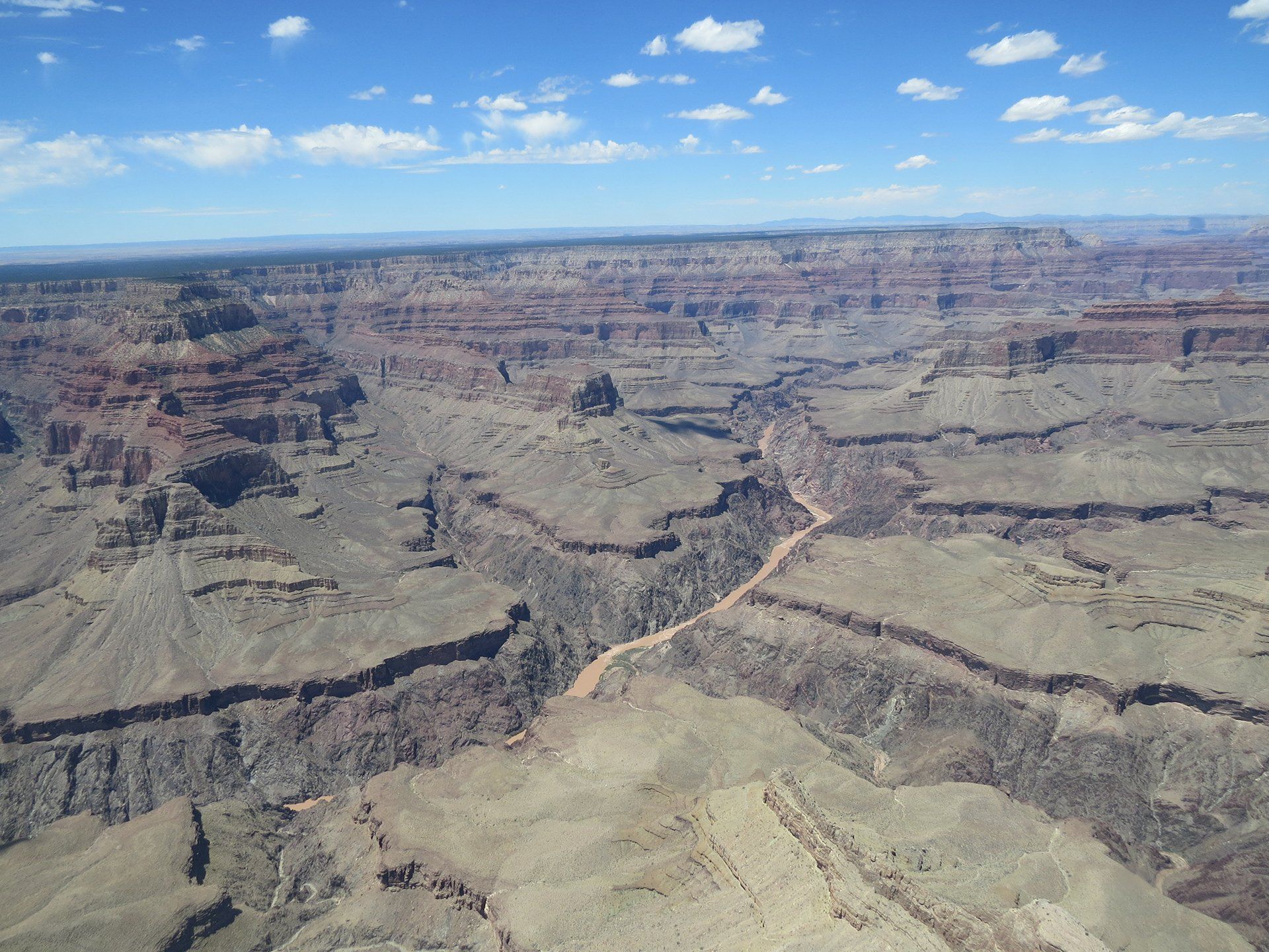 Uitzicht op de Grand Canyon met gelaagde rotsformaties, een blauwe hemel en een rivier die door de kloof kronkelt.