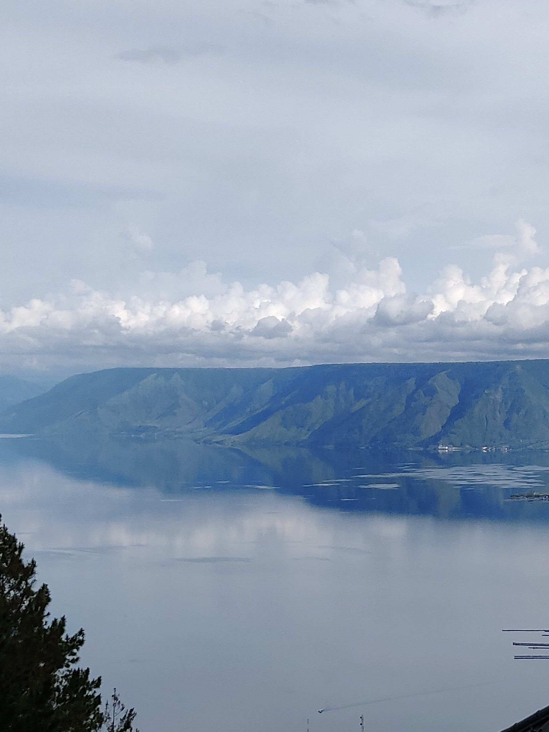 Het Tobameer in Indonesië, met een weerspiegeling van een bergketen onder een bewolkte hemel.