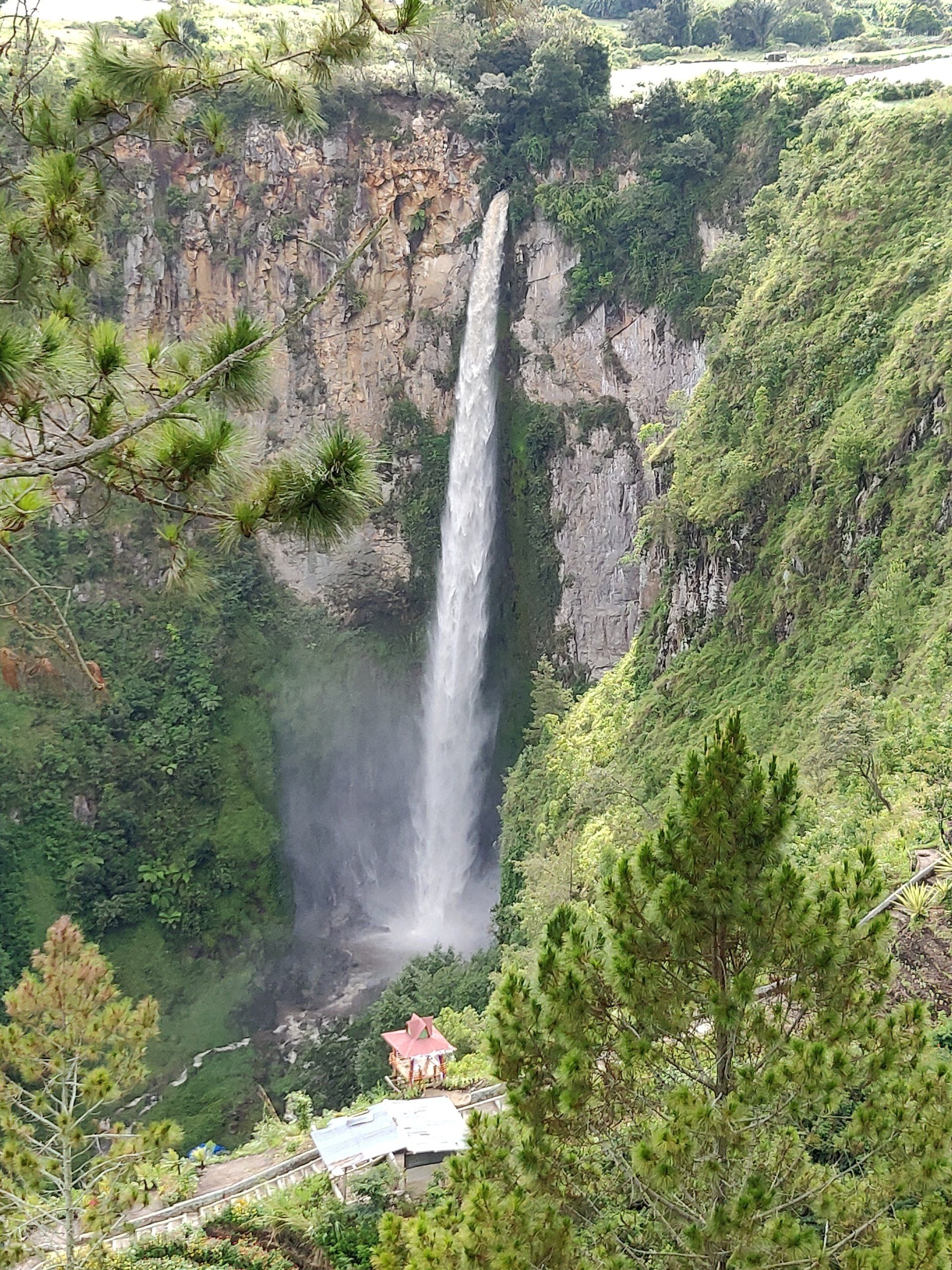 Een waterval die langs een klif naar beneden stort, omgeven door weelderige groene vegetatie.