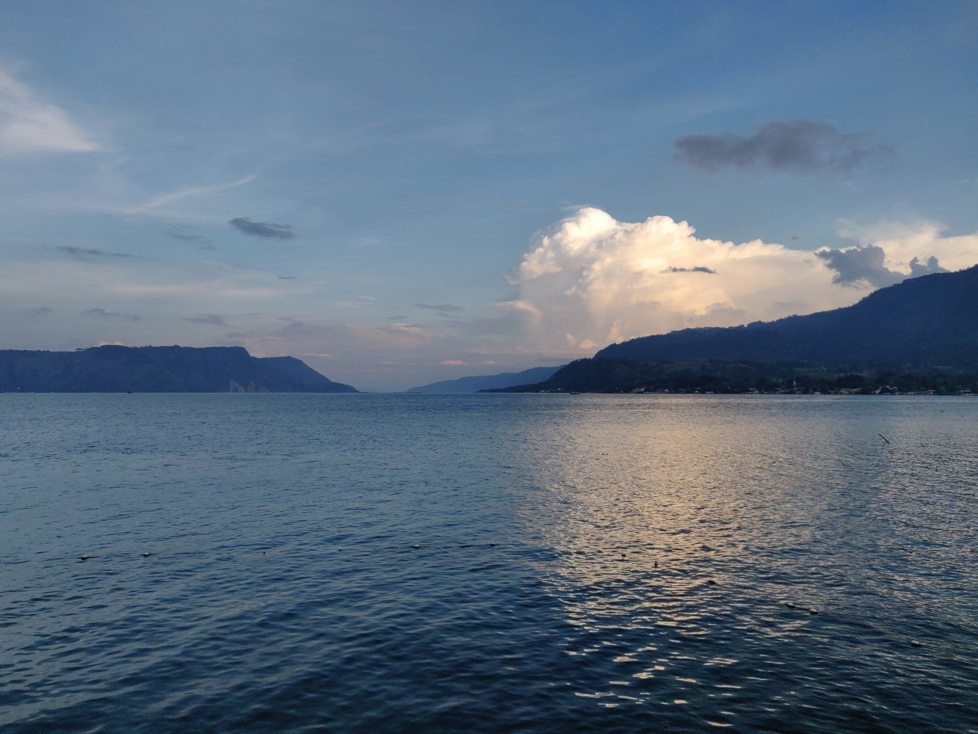Rustig water met bergen in de verte onder een bewolkte hemel.
