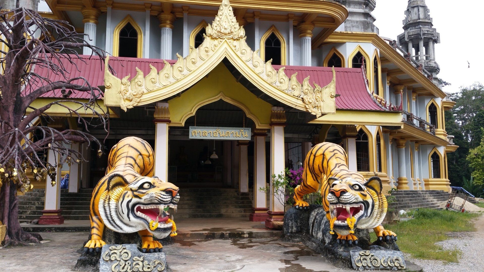 Twee tijgerbeelden flankeren de ingang van een tempel met een gouden dak.