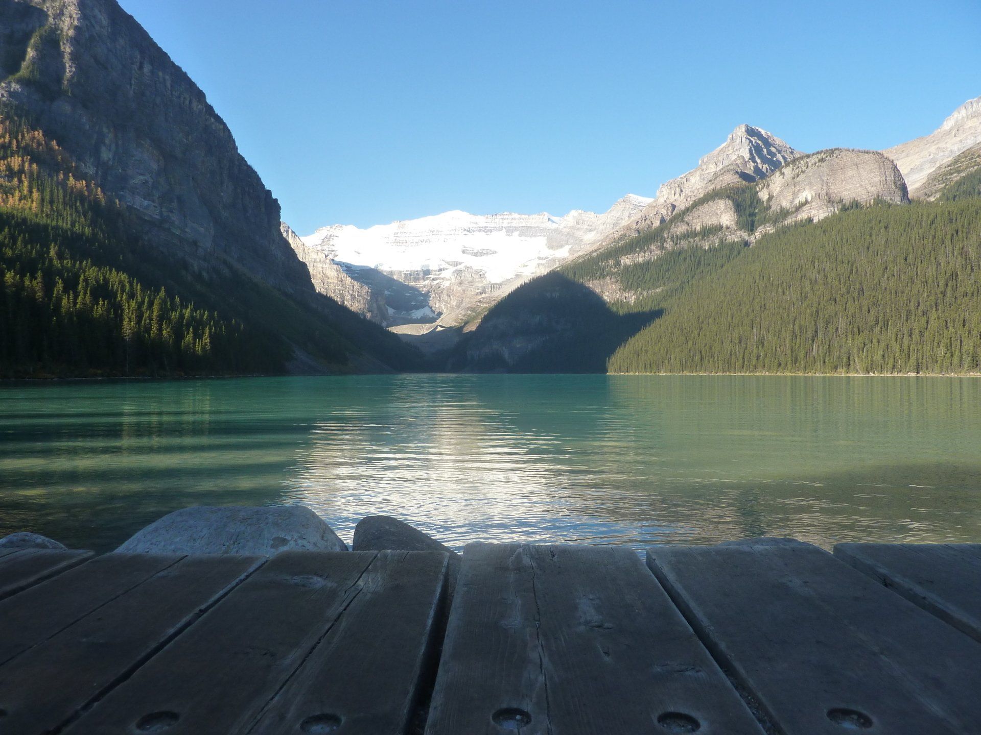 Lake Louise, omgeven door bergen onder een helderblauwe hemel, gezien vanaf een houten steiger.