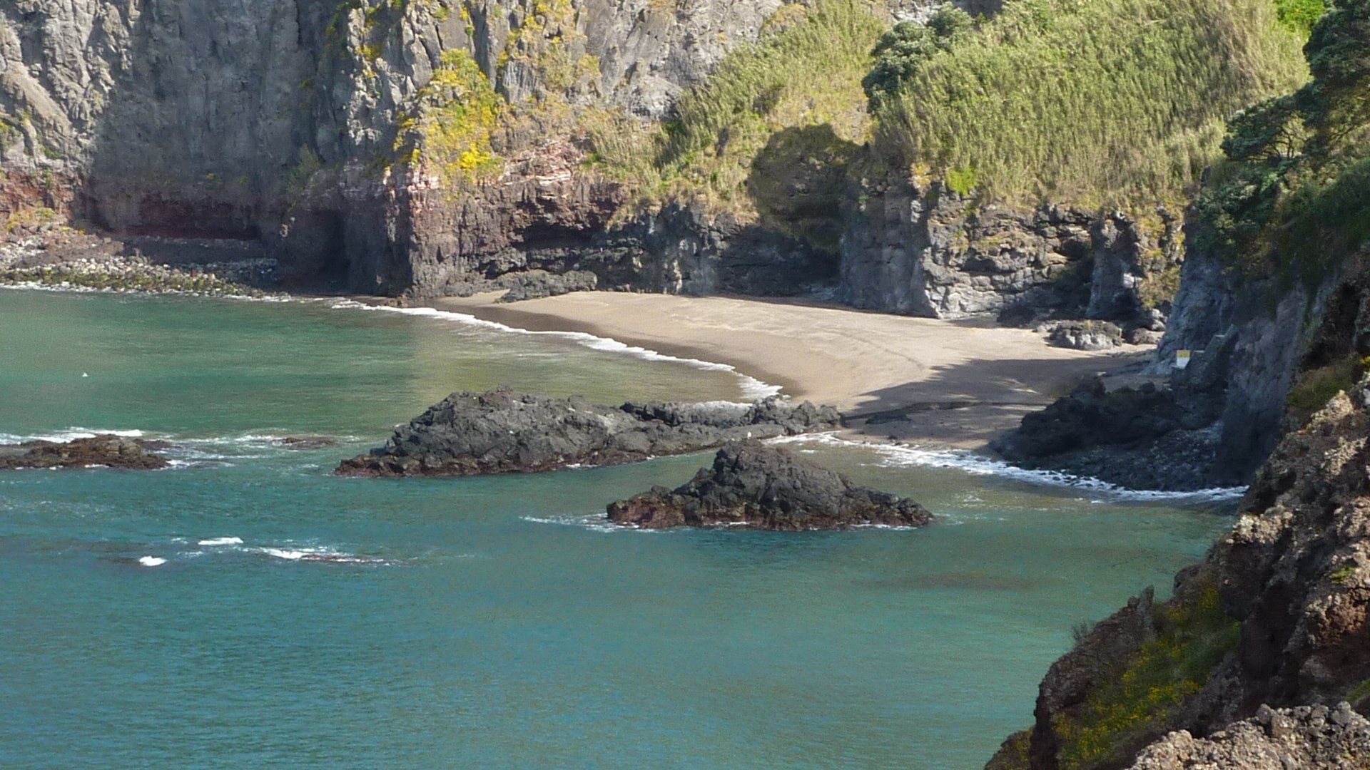 Rotsachtige baai met turquoise water, donkere rotsen en kliffen.