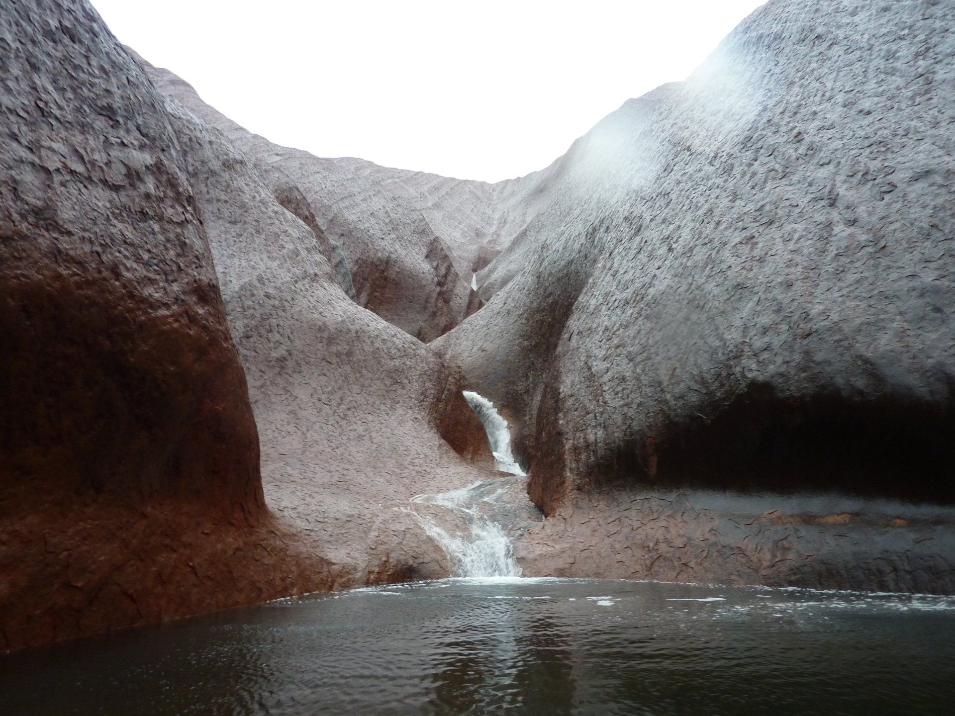 Een waterval die neerstort in een donkere poel in de rode rotswanden van een kloof.