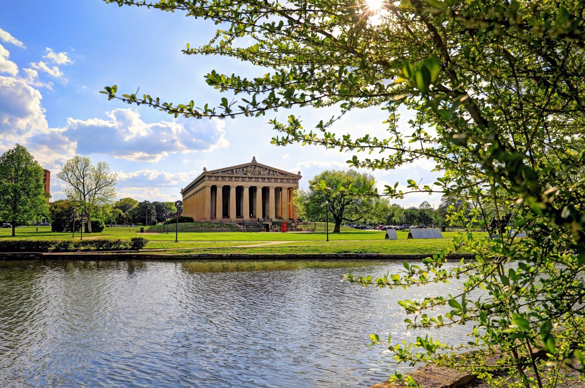 Het Parthenon in Nashville, Tennessee, omlijst door bomen en weerspiegeld in een meer onder een zonnige hemel.