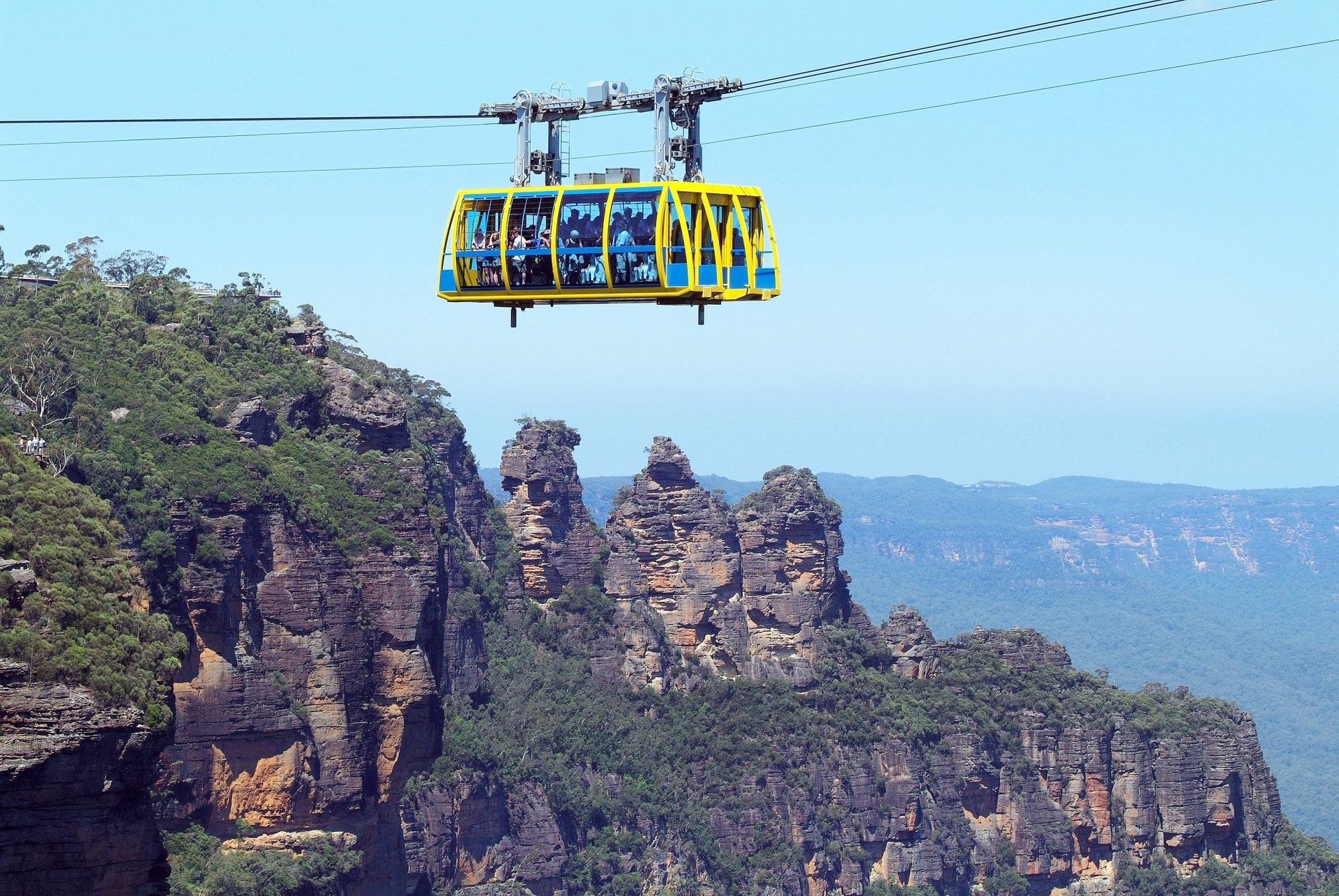 Een gele kabelbaan met passagiers rijdt over de rotsformatie Three Sisters in de Blue Mountains.