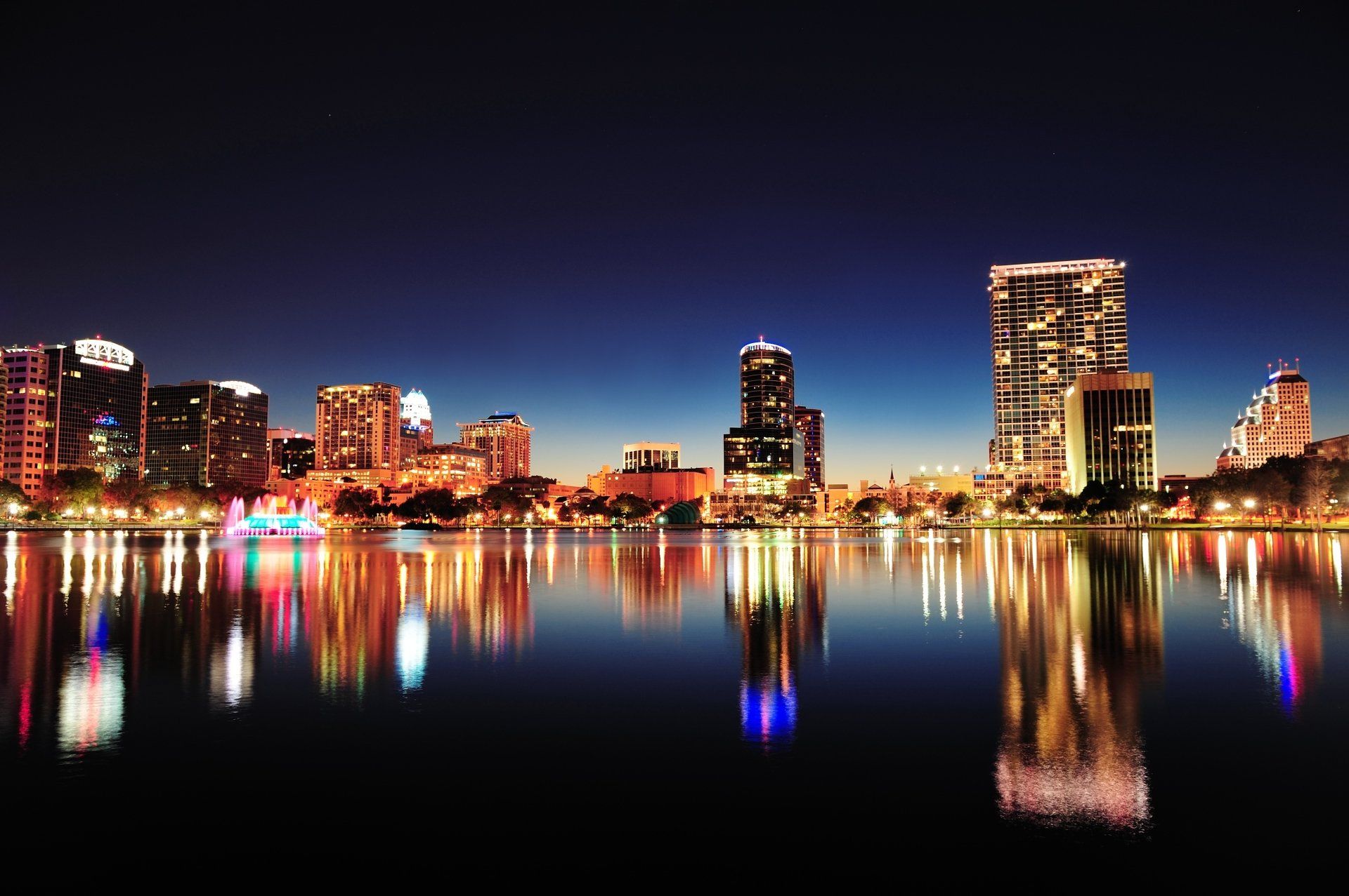 De skyline van Orlando weerspiegelt zich 's nachts in het kalme water. De stadslichten zorgen voor kleurrijke reflecties.