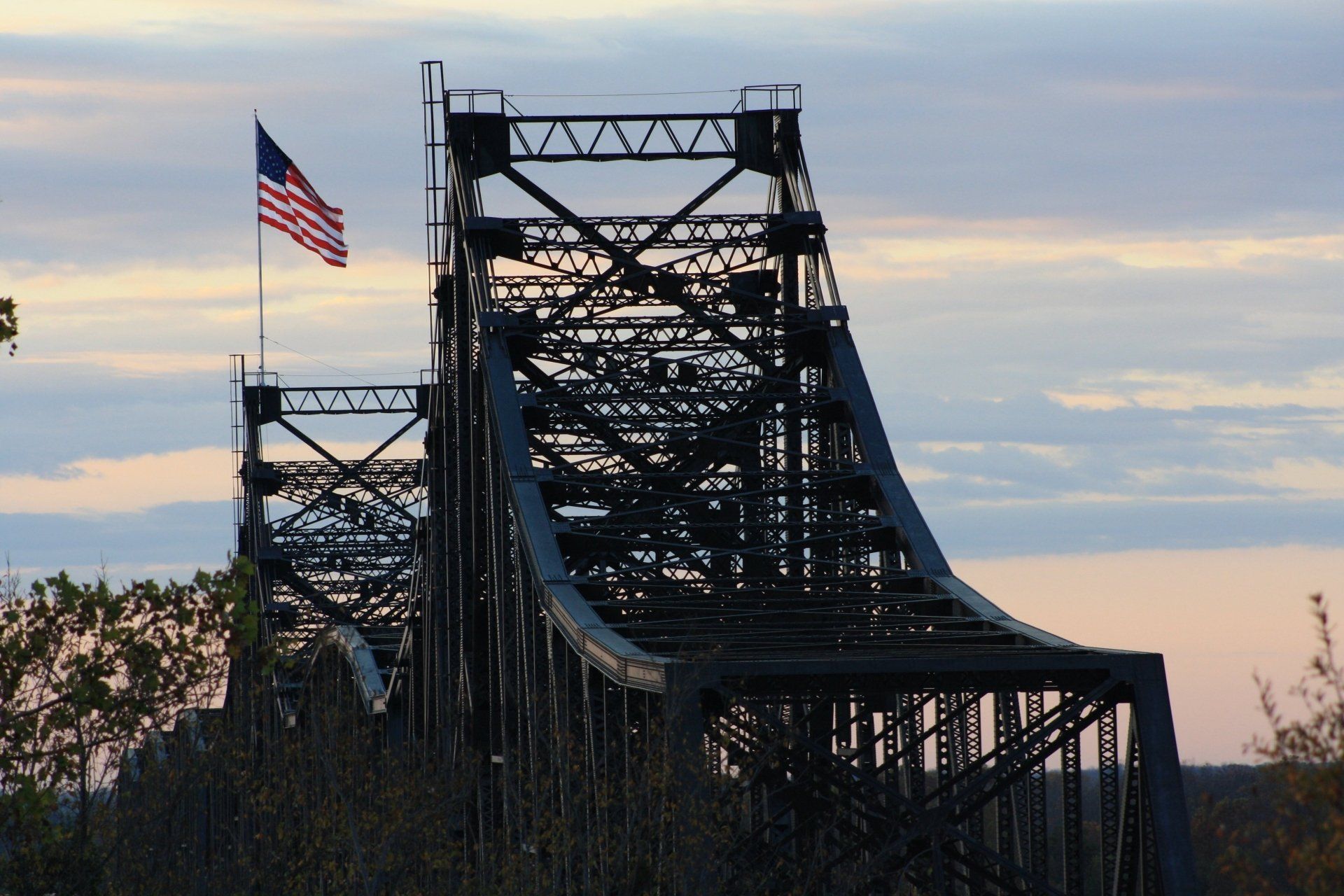 Silhouet van een brug met de Amerikaanse vlag op de achtergrond, in de schemering.