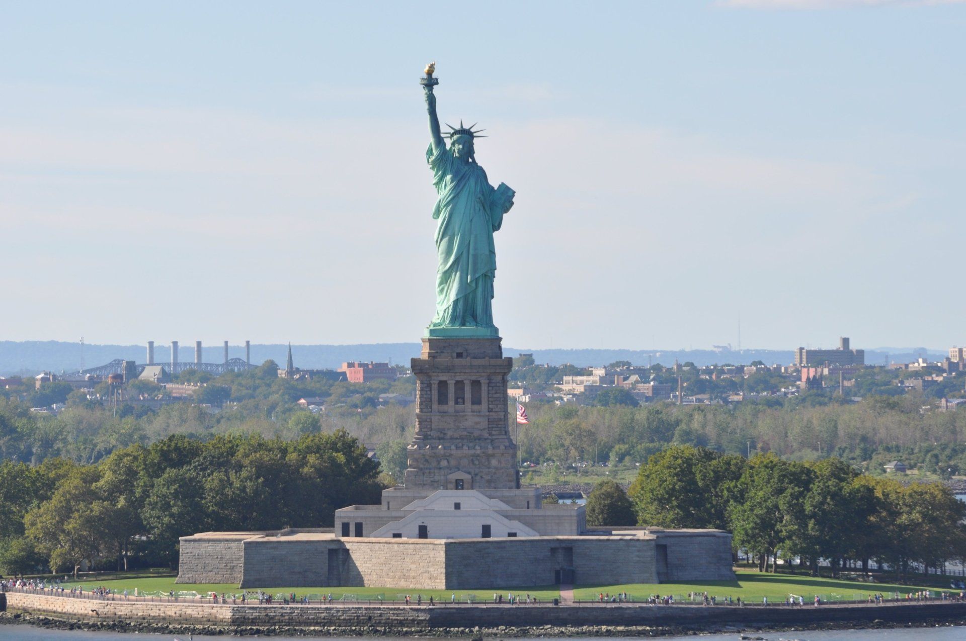 Het Vrijheidsbeeld op Liberty Island in New York City staat fier, groen met uitgestrekte arm, tegen een blauwe hemel.