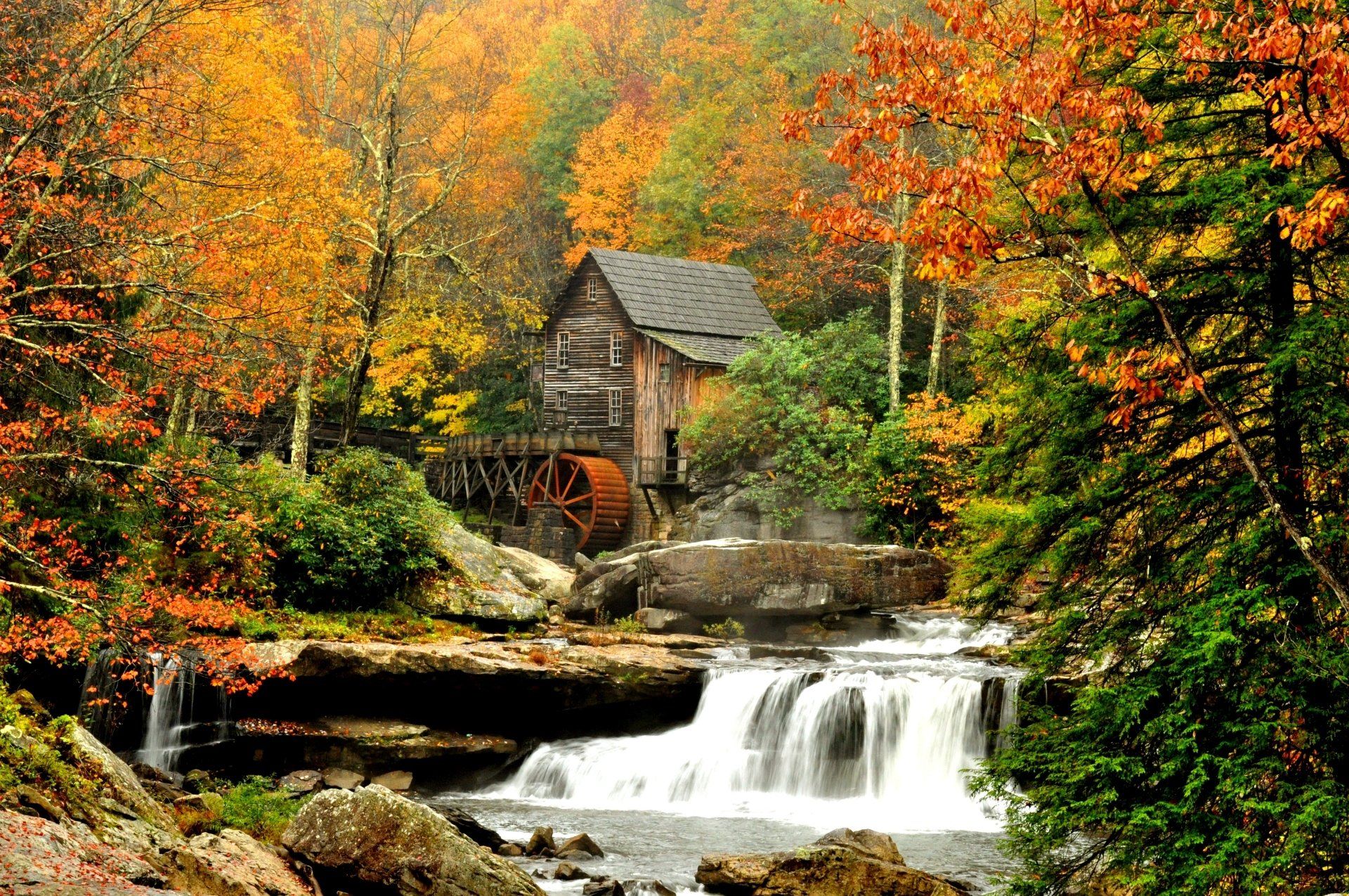 Herfsttafereel: Watermolen bij een waterval, omgeven door kleurrijk gebladerte.
