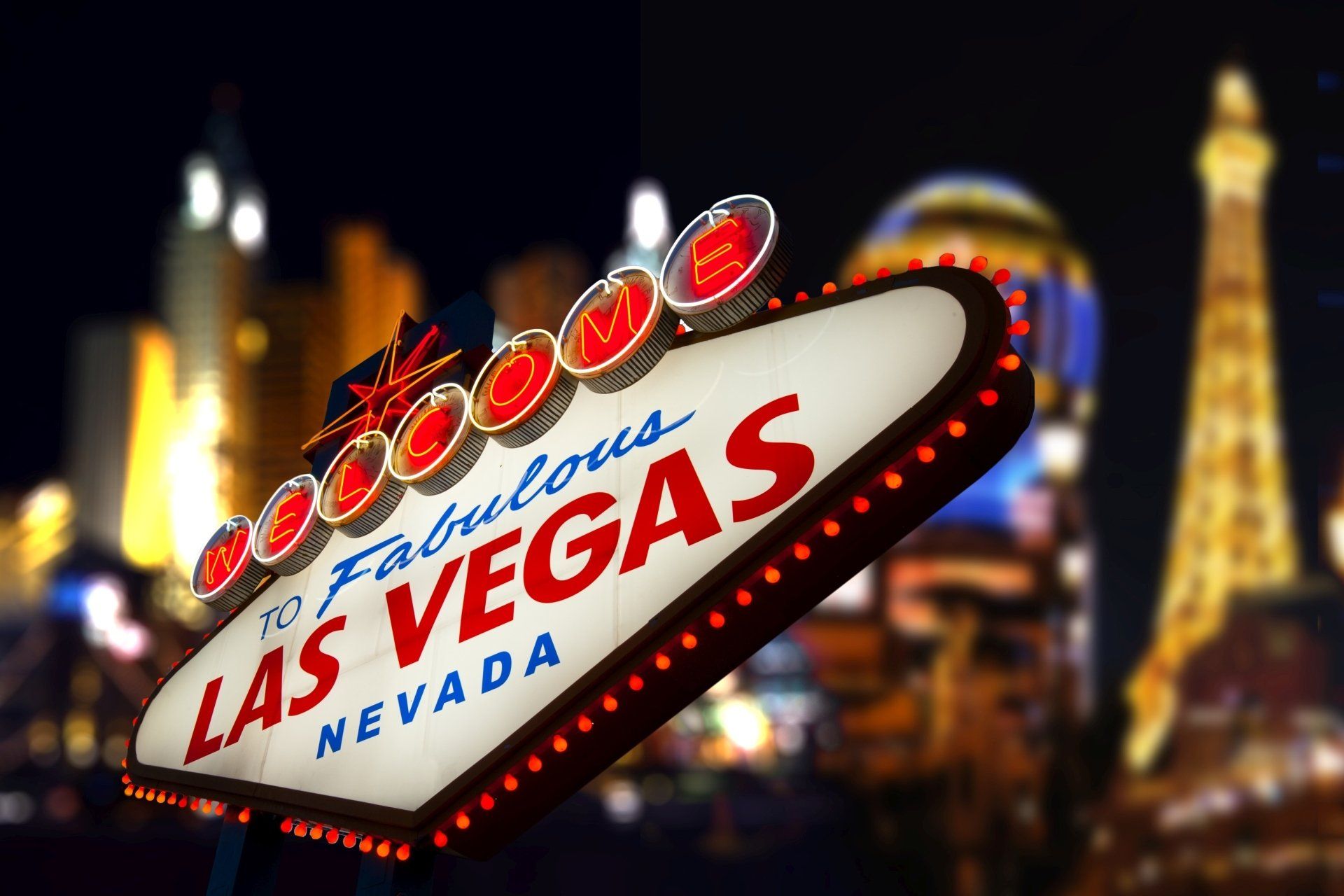 Het Las Vegas-bord is 's nachts verlicht, met de stadslichten op de wazige achtergrond.