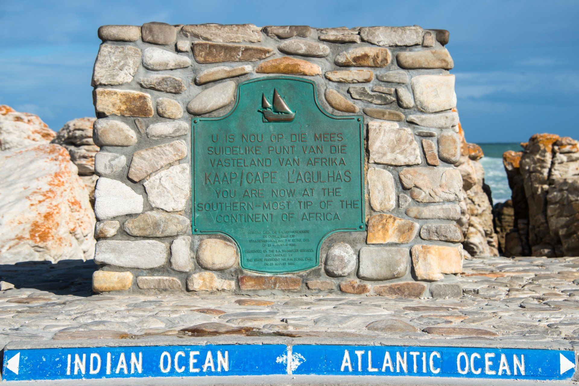 Stenen monument dat het punt markeert waar de Indische en Atlantische Oceaan samenkomen, met een plaquette en een bord.