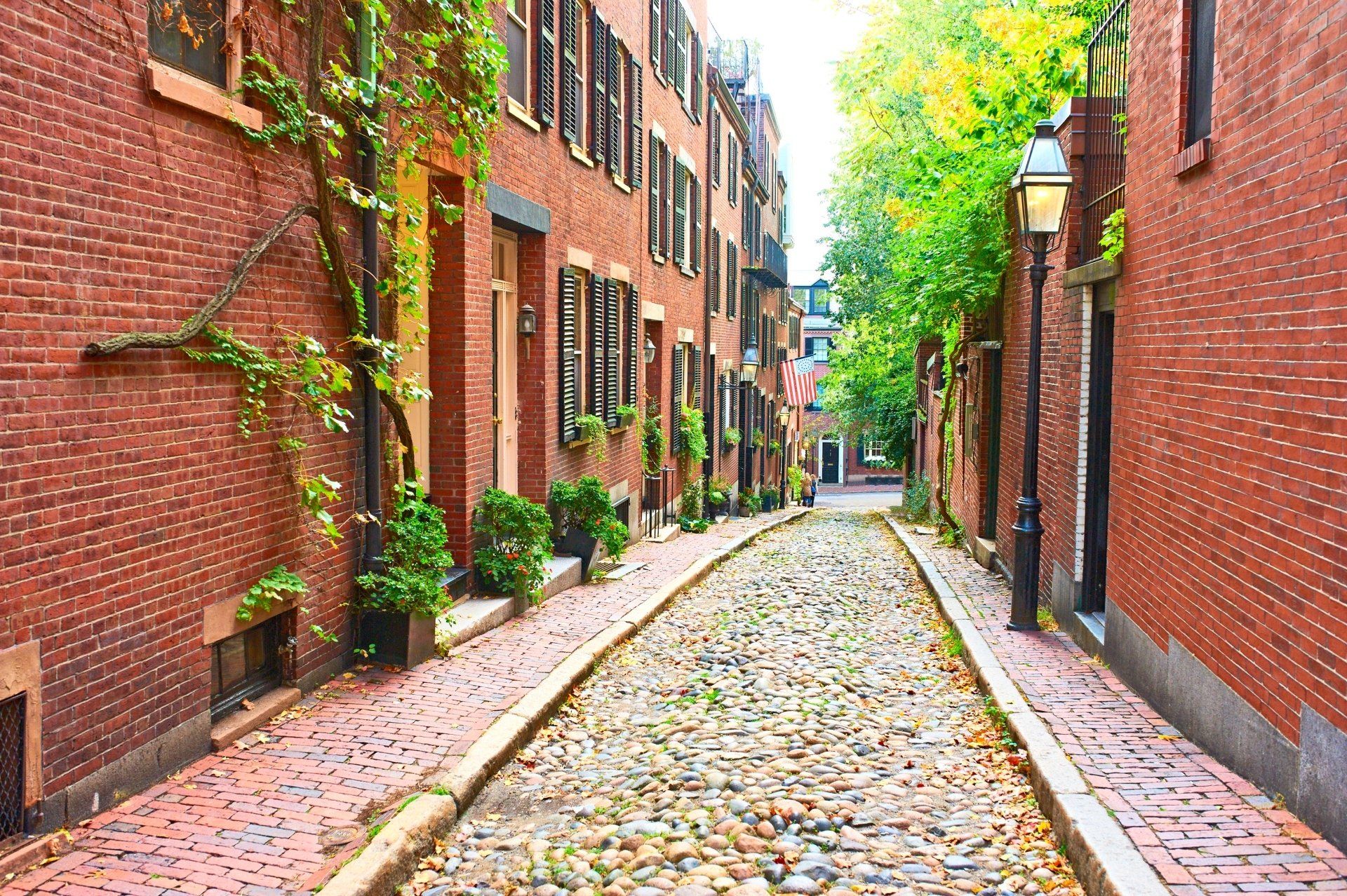 Een straat met kinderkopjes in Boston, omzoomd door rode bakstenen gebouwen en bomen.