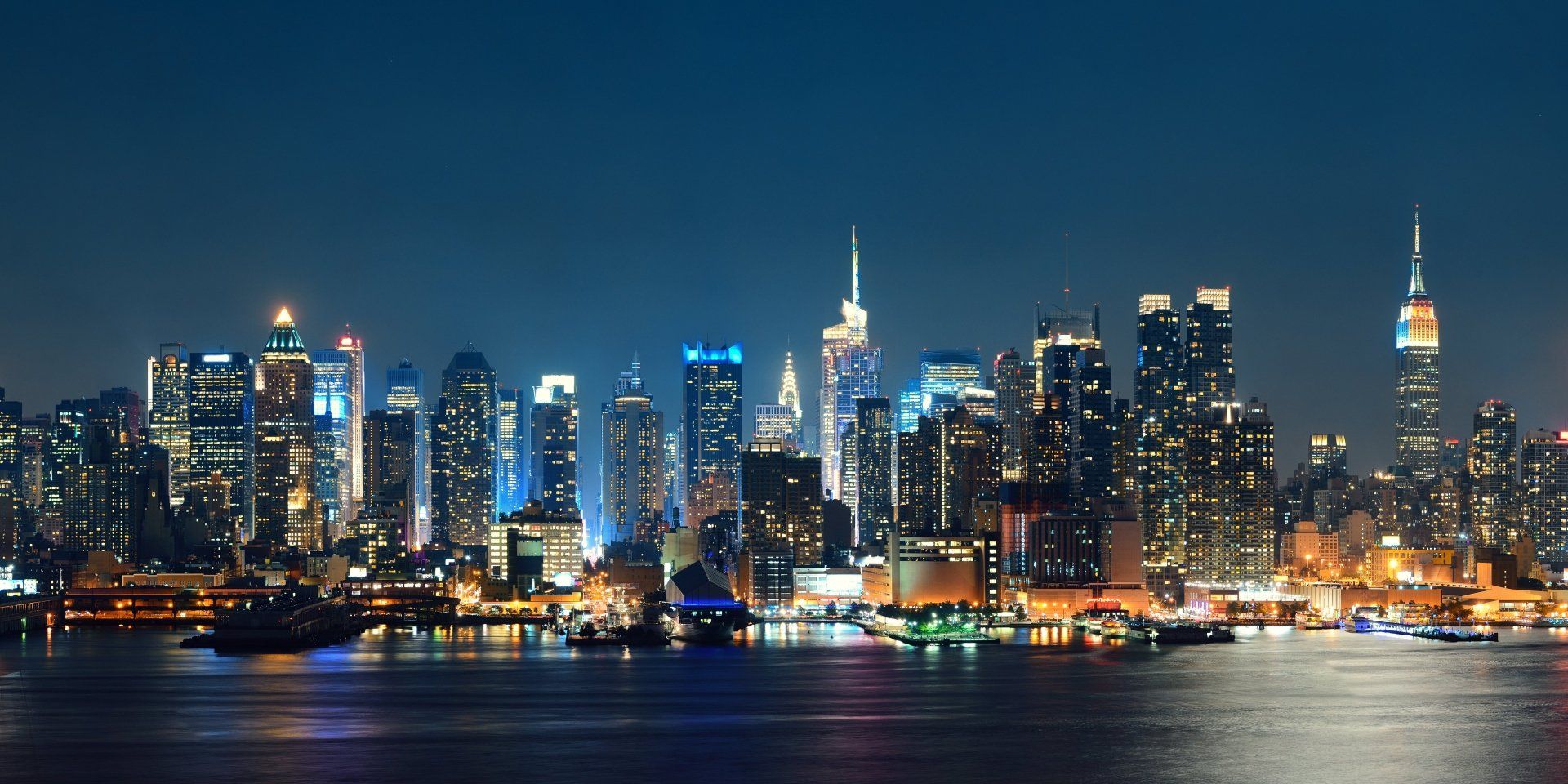 Nachtelijk uitzicht op de skyline van een stad met verlichte gebouwen die weerspiegelen in het donkere water.