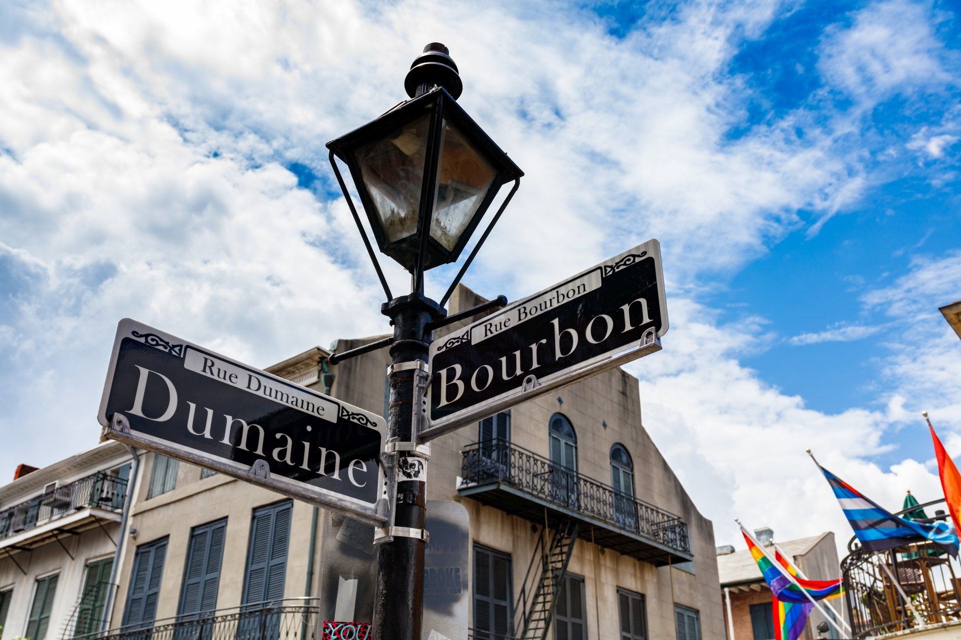 Straatnaamborden voor Dumaine en Bourbon in New Orleans, met een lantaarnpaal en een gebouw op de achtergrond.