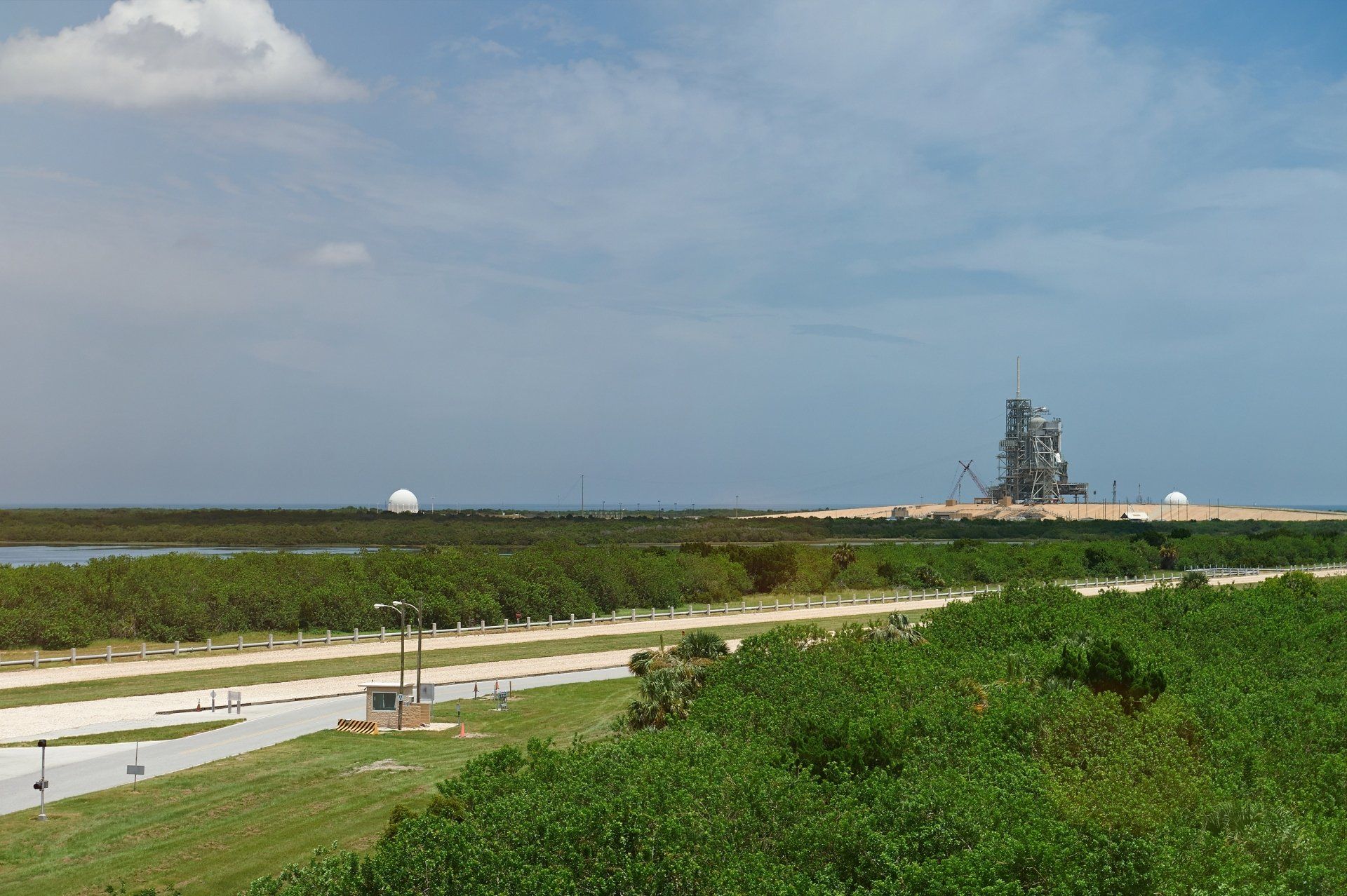 Een vergezicht op een lanceercomplex met een spaceshuttle, een grasveld op de voorgrond en een blauwe lucht.