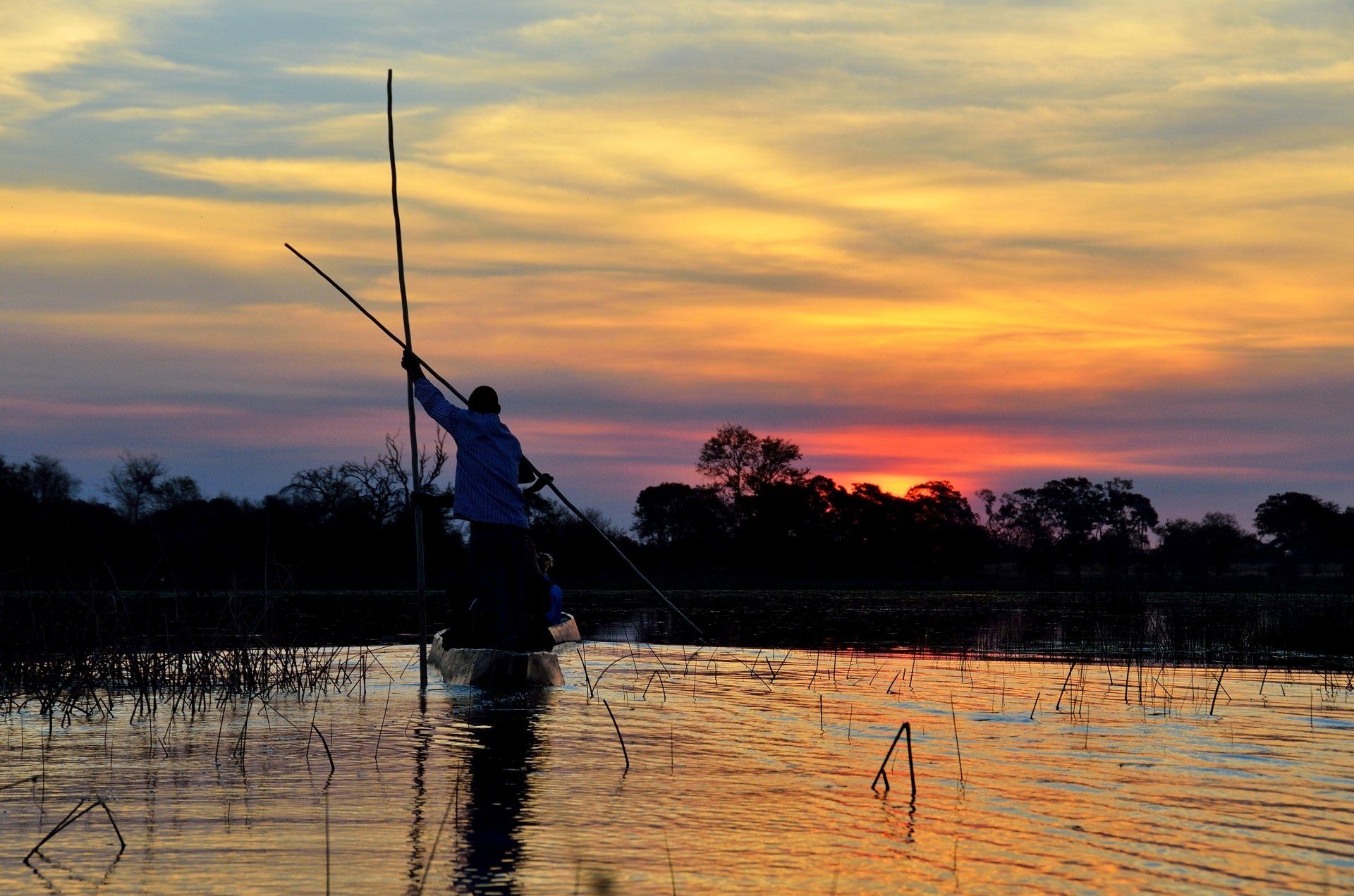 Man in een boot bij zonsondergang; hij houdt een hengel vast, zijn silhouet steekt af tegen het water met een levendige lucht.
