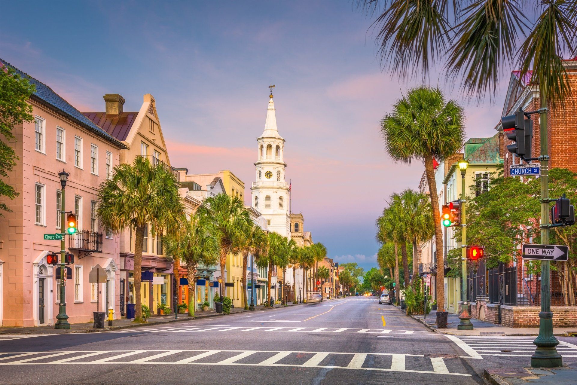 Straat in Charleston, South Carolina, met palmbomen langs de weg, historische gebouwen en een kerktoren aan het einde.