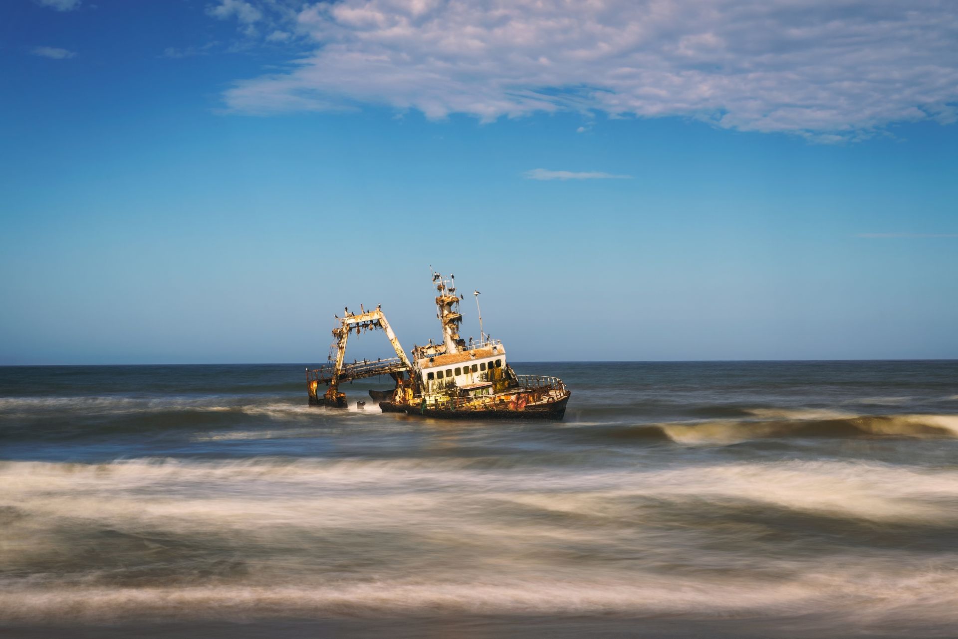 Scheepswrak in de oceaan; wit en bruin schip aan de horizon tegen een blauwe hemel en golven.