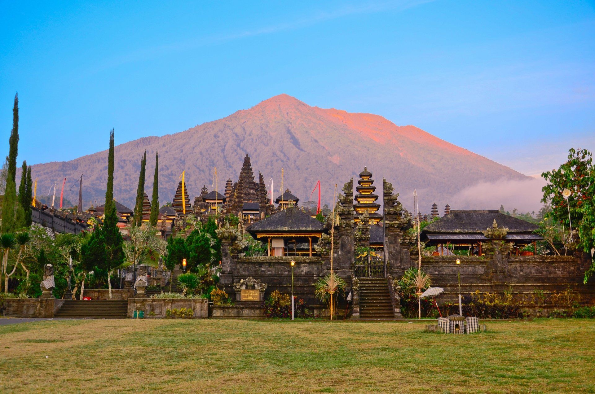 Tempelcomplex met berglandschap op de achtergrond, Bali, Indonesië. Groen gras, donkere stenen bouwwerken en een blauwe lucht.