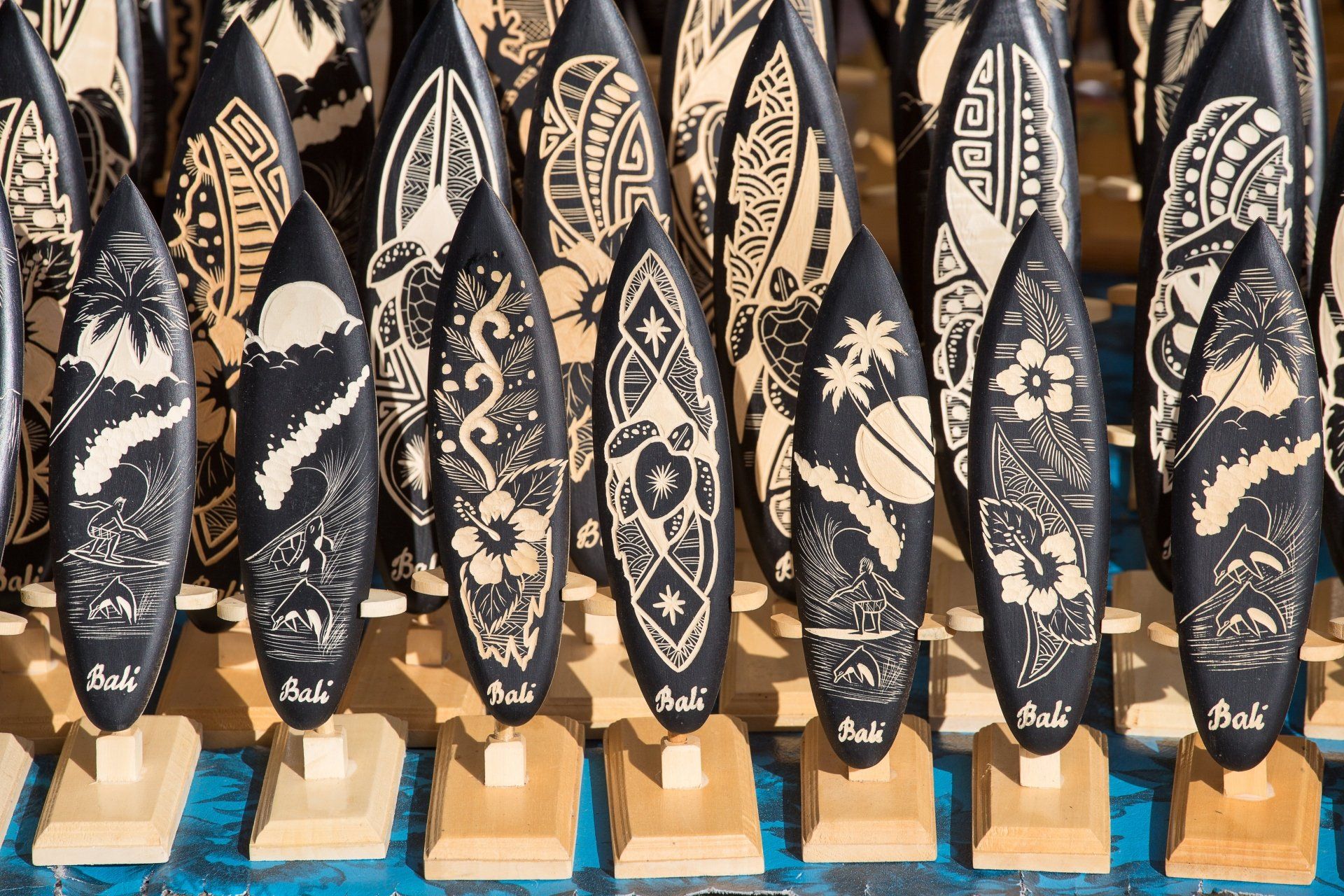Rijen kleine zwarte houten surfplanken met ingesneden witte versieringen staan tentoongesteld.