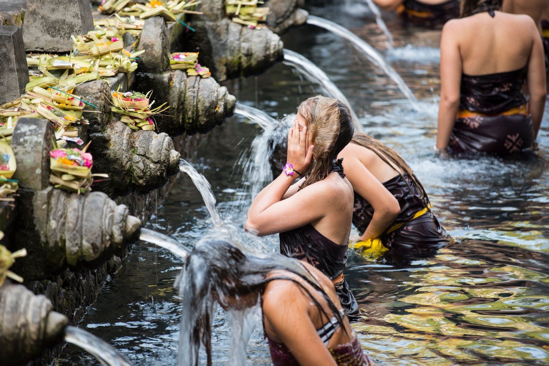 Mensen baden onder waterfonteinen in een stenen bassin. Sommigen bedekken hun gezicht. Bali, Indonesië.