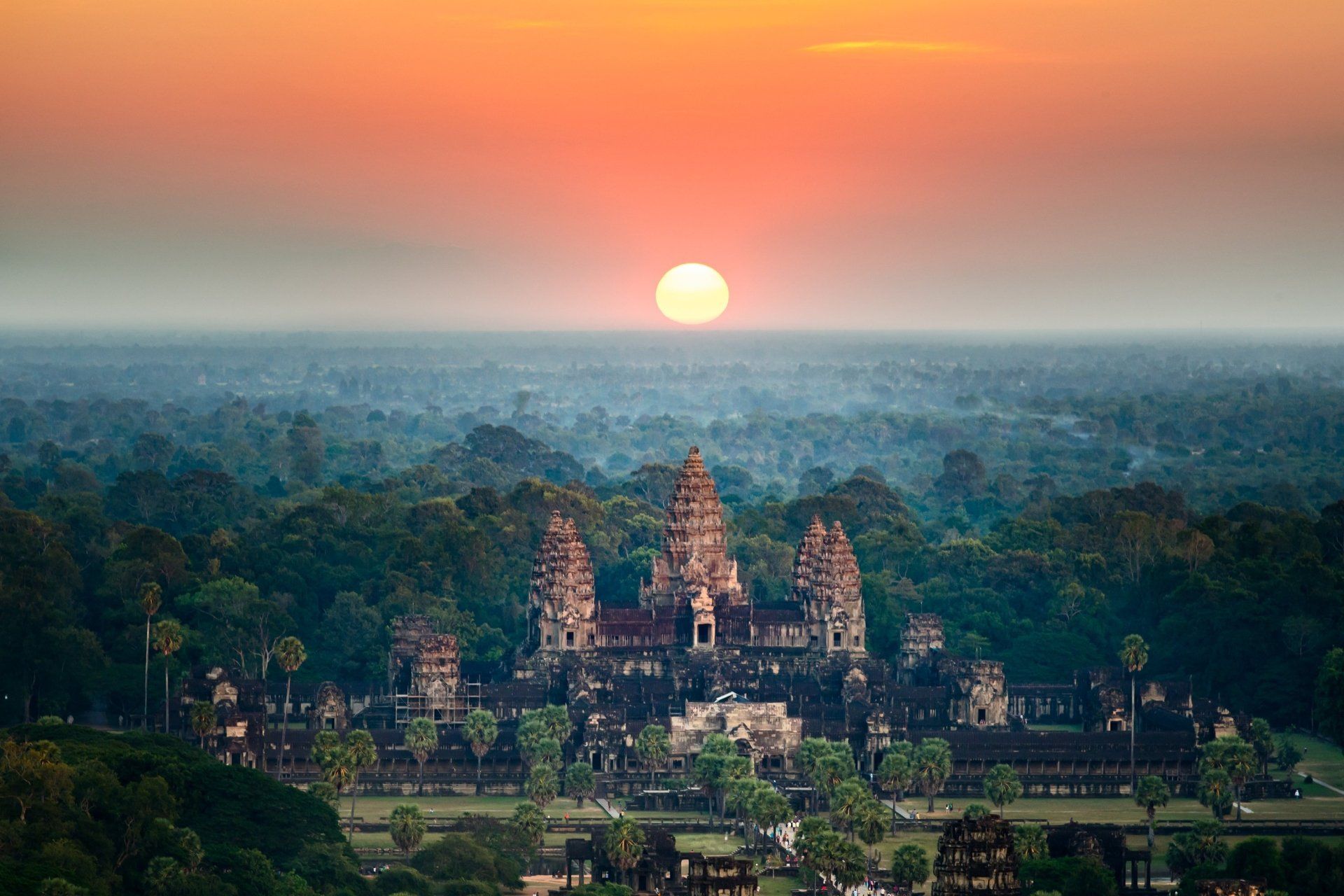 De Angkor Wat-tempel bij zonsopgang; een oranje hemel boven weelderige groene bomen.