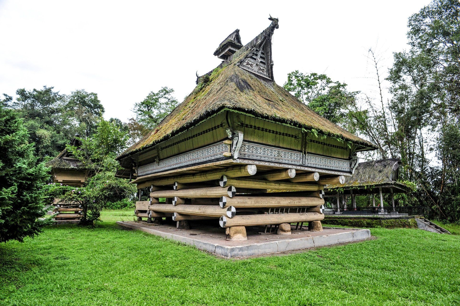 Traditioneel Indonesisch huis met een verhoogde houten constructie en een rieten dak, omgeven door groen gras en bomen.