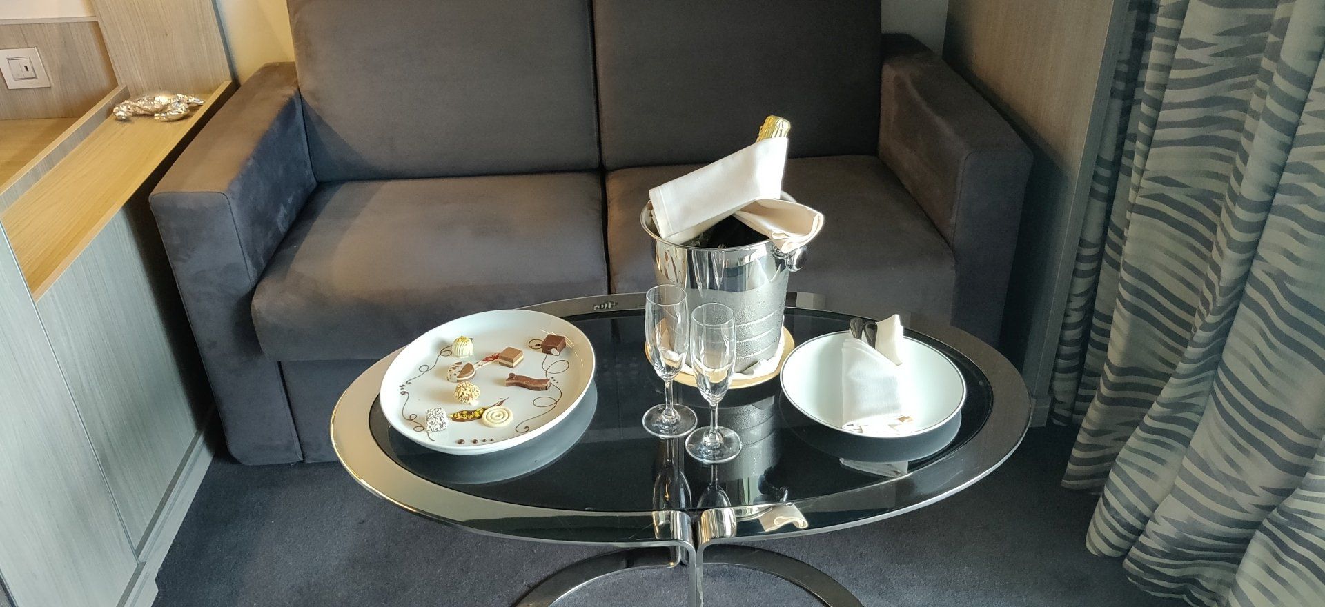 Een klein tafeltje met twee borden en een flessenhouder voor een bank. Rechts hangen de gordijnen.
