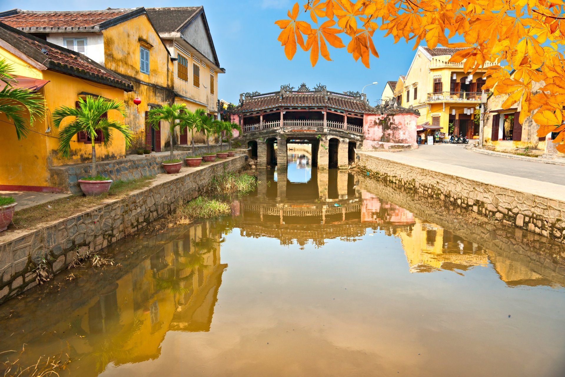 Hoi An, een oude stad in Vietnam, met een brug die weerspiegeld wordt in het kalme water, gele gebouwen en herfstbladeren.