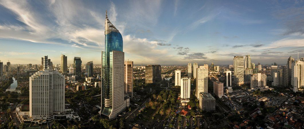 De skyline van Jakarta met wolkenkrabbers en blauwe glazen gebouwen tegen een bewolkte hemel.