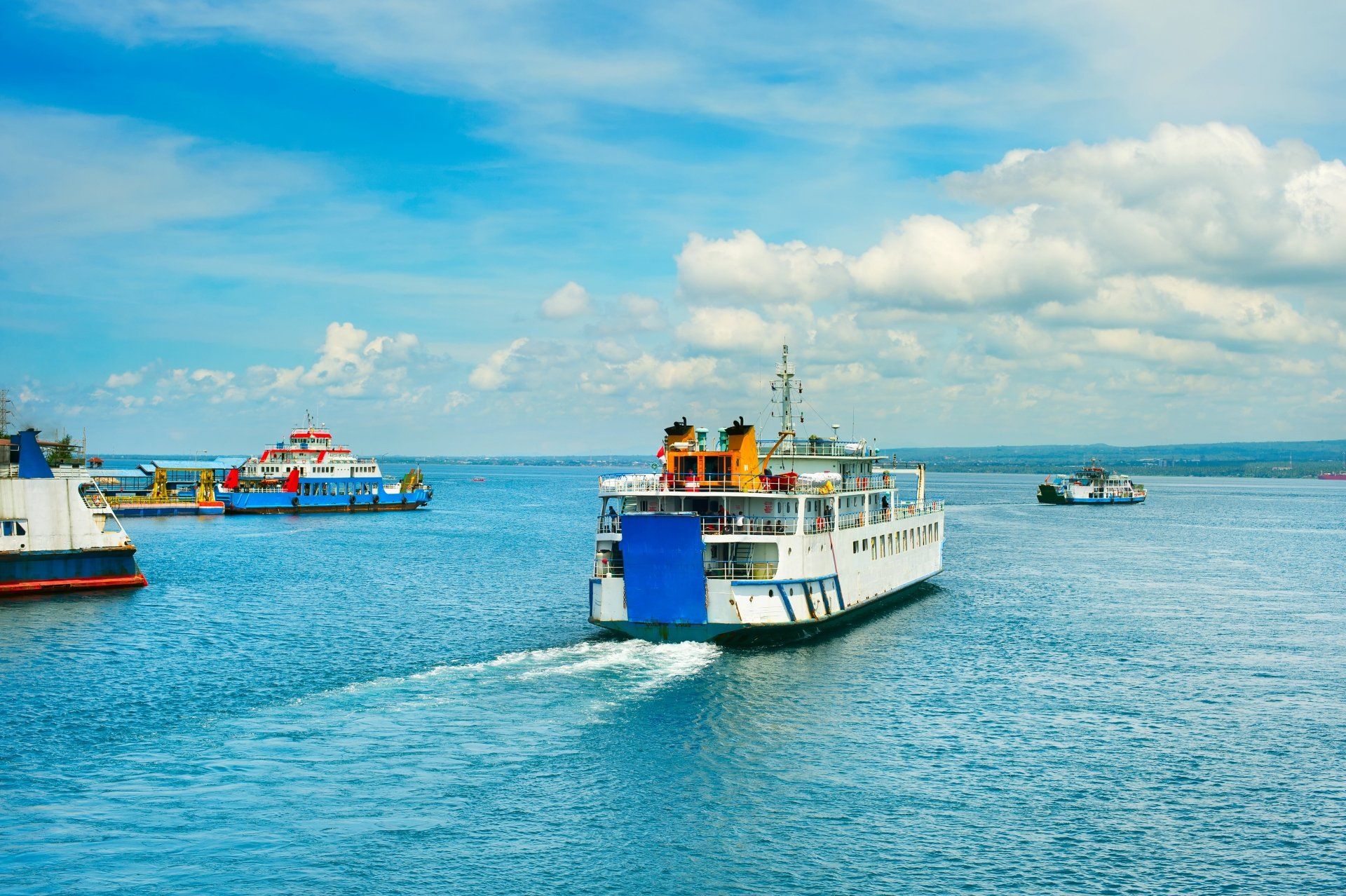 Verschillende veerboten op een helderblauwe zee onder een gedeeltelijk bewolkte hemel.