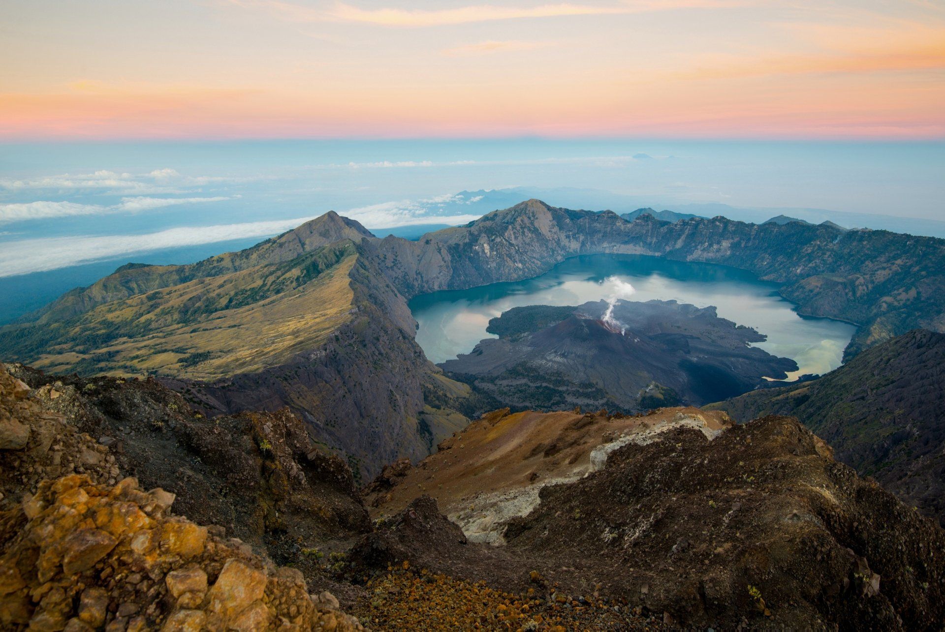 Vulkanische caldera met een meer, rotsachtig terrein en een blauw-oranje lucht.