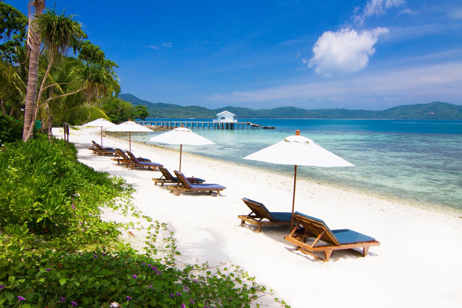 Wit zandstrand met ligstoelen, parasols en helderblauw water.