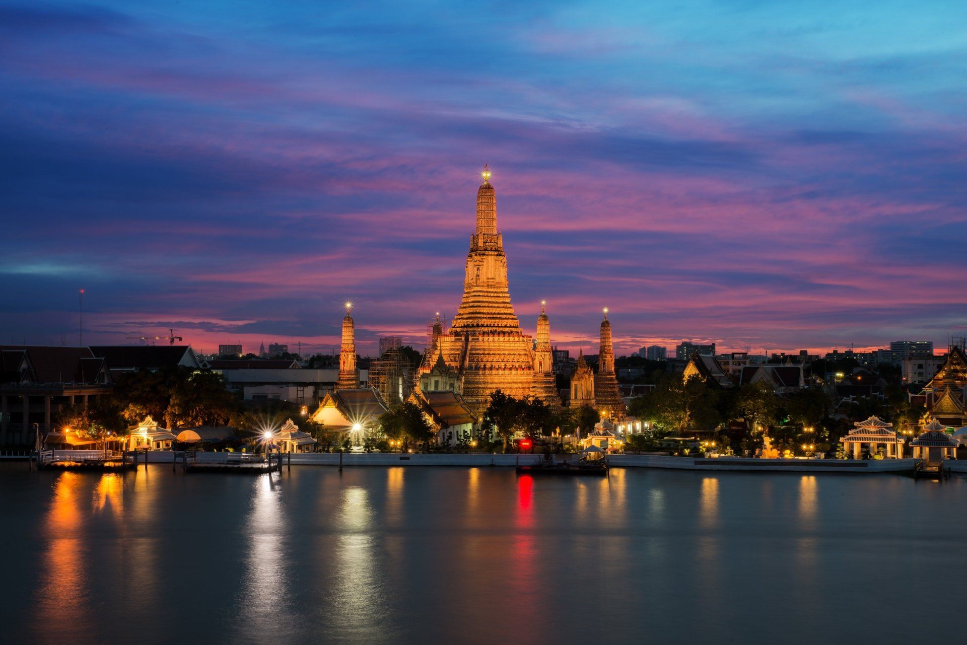 De Wat Arun-tempel in Bangkok, Thailand, is bij schemering verlicht en de kleuren van de hemel weerspiegelen zich in de rivier.