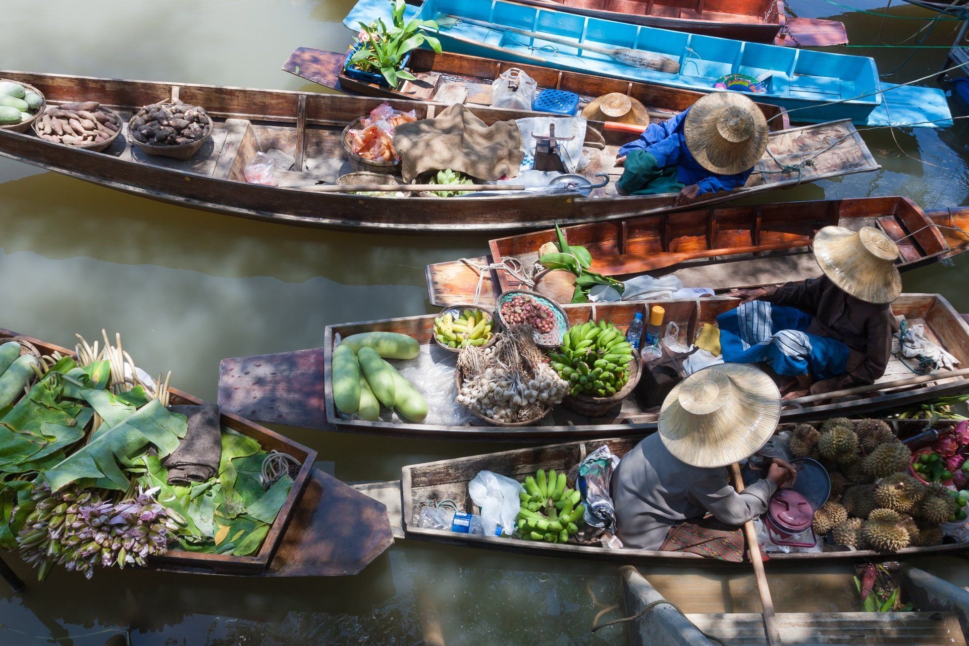 Boten volgeladen met producten op een drijvende markt; verkopers met strohoeden peddelen.