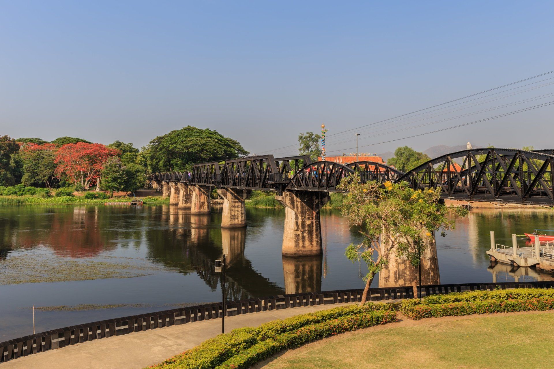 Brug over de rivier Kwai met een zwarte ijzeren constructie, betonnen steunpilaren en een heldere hemel in Kanchanaburi, Thailand.