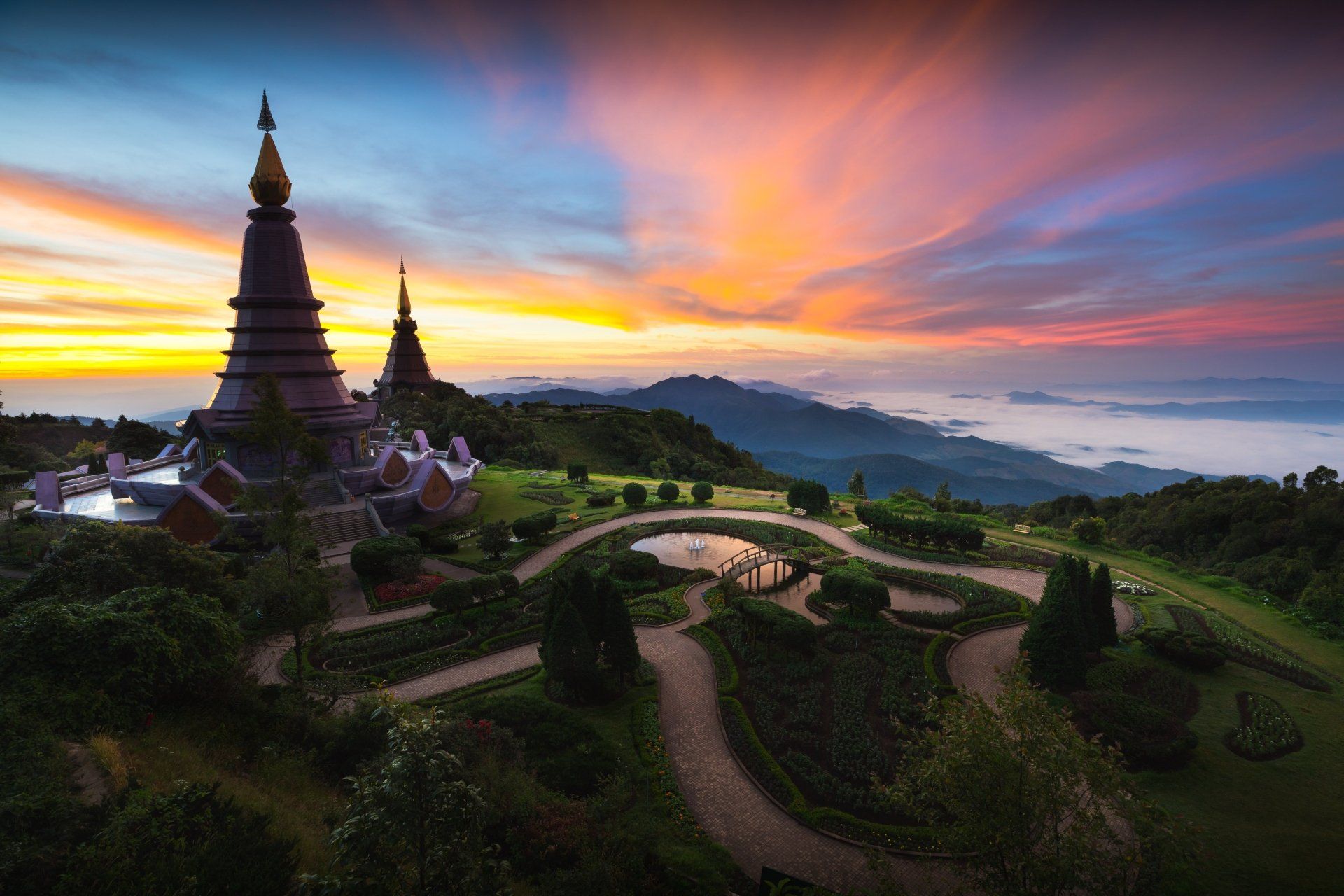 Twee pagoda's met meerdere verdiepingen bovenop een berg bij zonsondergang, met een kleurrijke hemel en paden.