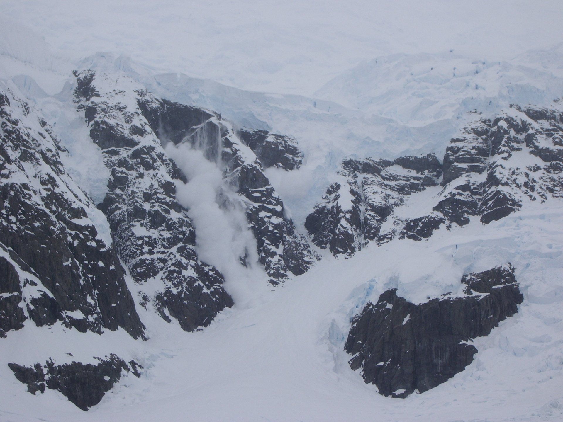 Besneeuwd berglandschap; een lawine van sneeuw en ijs die langs een rotswand naar beneden stort.