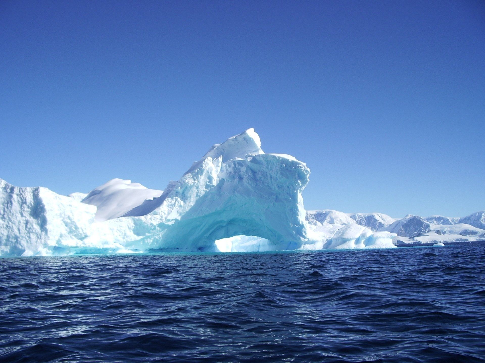 Blauwe ijsberg met een grote boog in de Antarctische oceaan onder een heldere hemel.