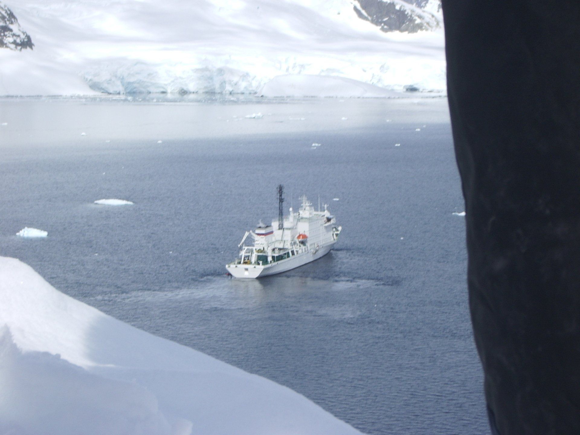 Wit schip op donker water, bergen en ijs op de achtergrond.
