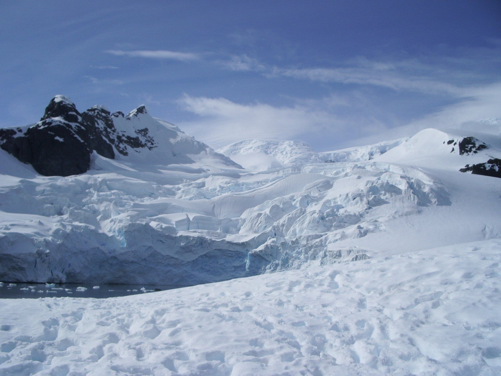 Besneeuwd Antarctisch landschap met gletsjer, bergen en blauwe lucht.