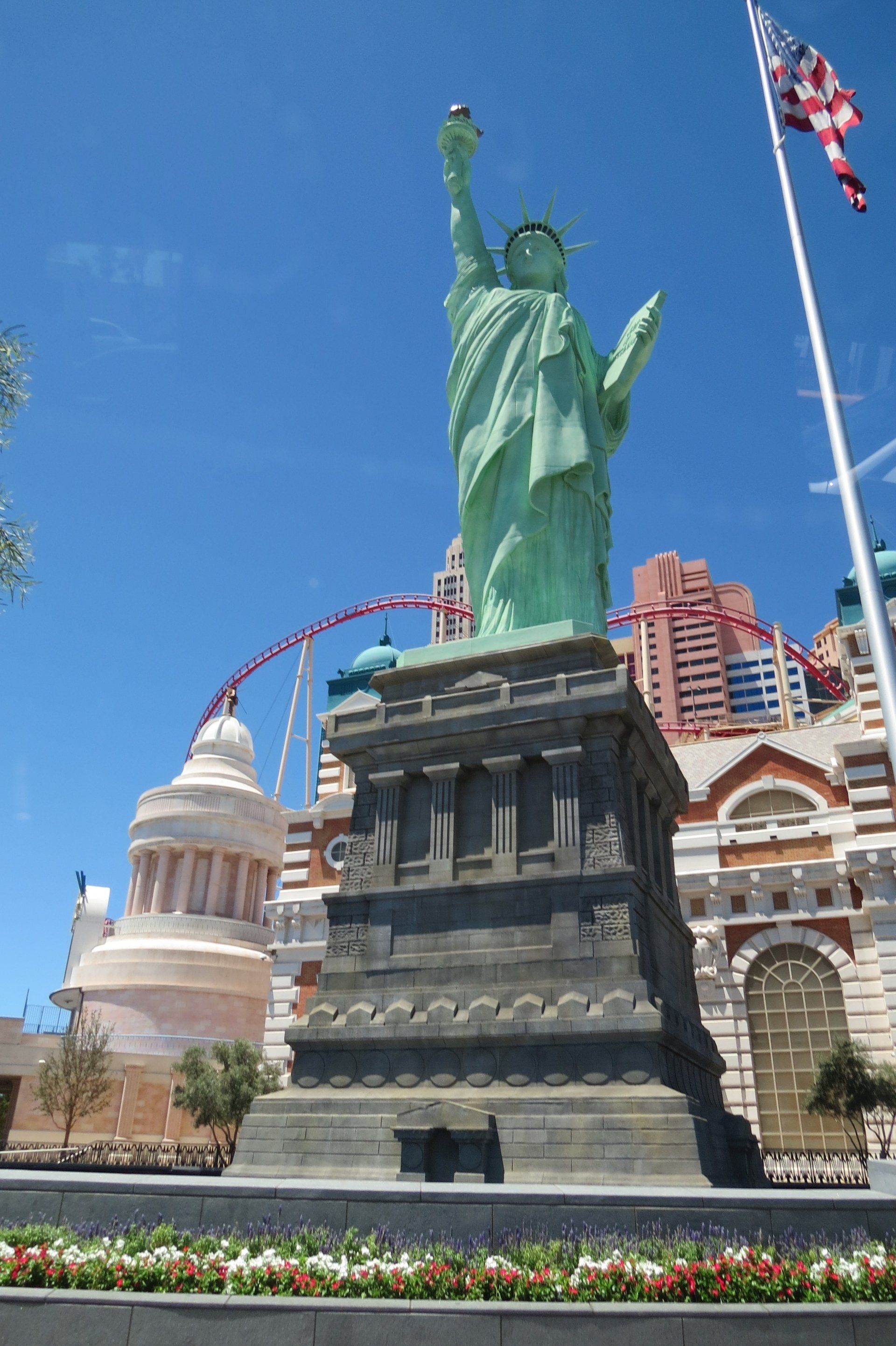 Replica van het Vrijheidsbeeld bij het New York-New York Hotel & Casino in Las Vegas, met een blauwe lucht en een achtbaan op de achtergrond.