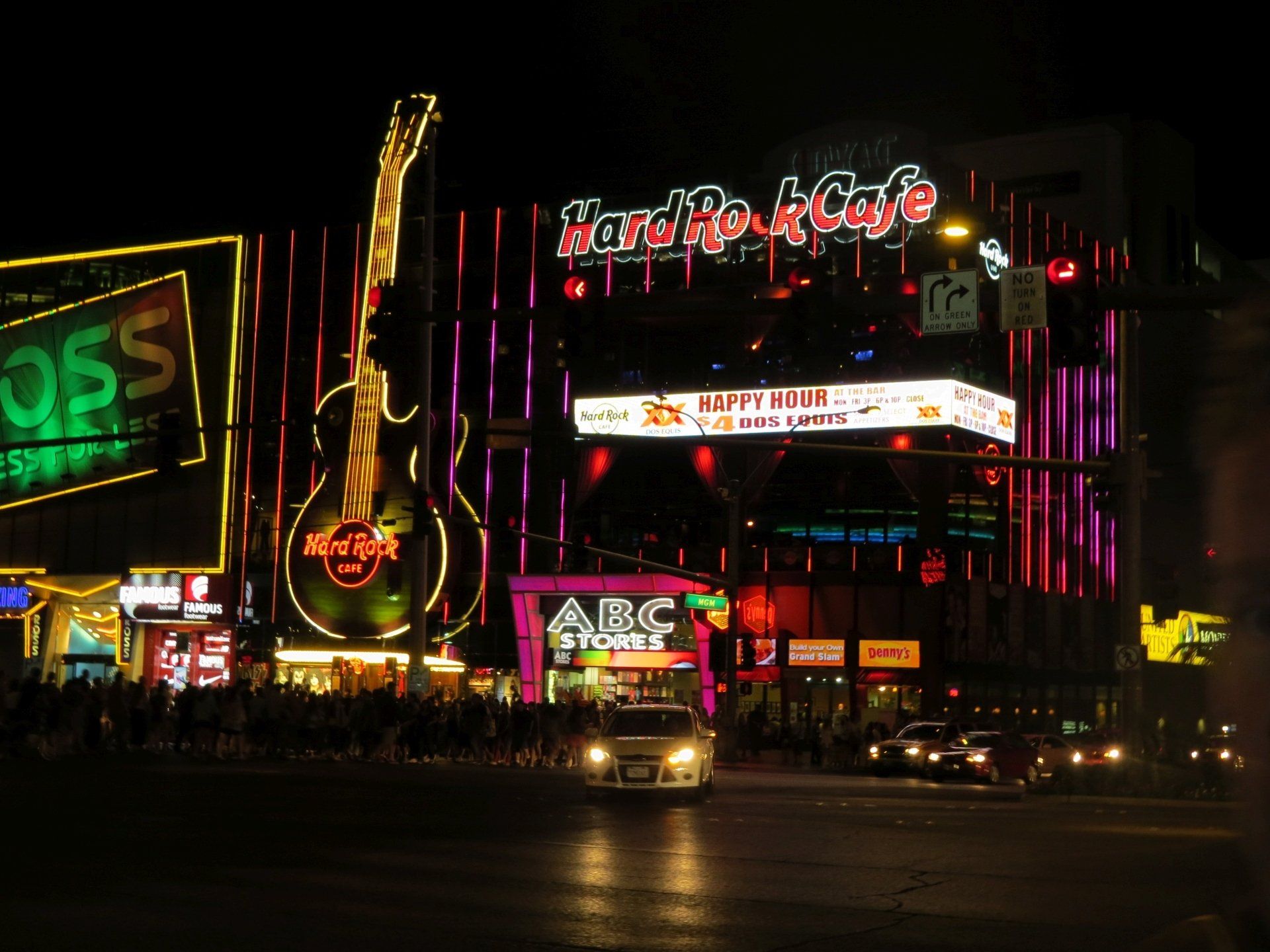 Het Hard Rock Cafe-gebouw 's nachts met verlichte gitaar, neonreclames en verkeer op straat.