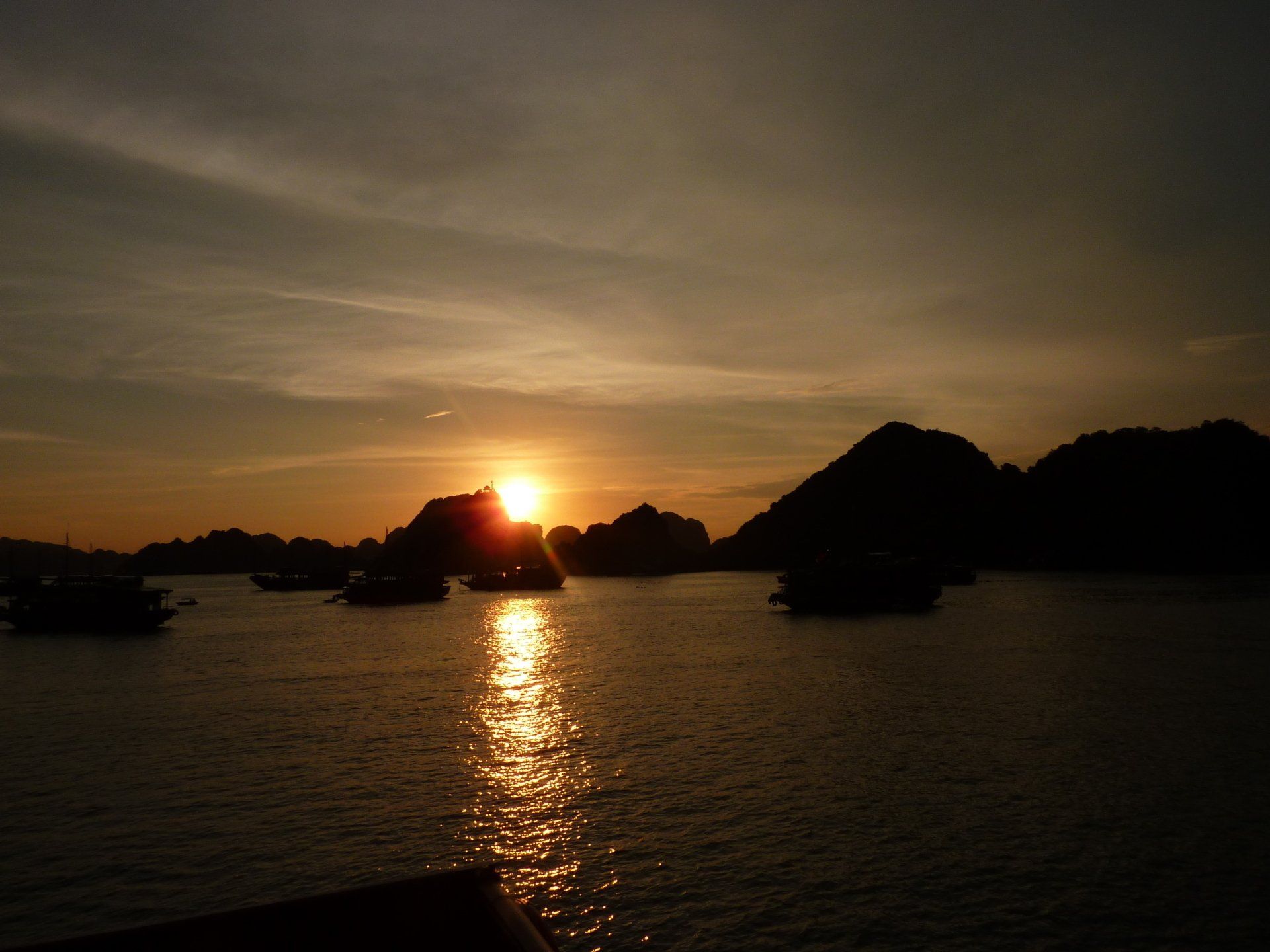 Zonsondergang boven het water met silhouetten van eilanden en boten. Gouden zonlicht weerkaatst op het wateroppervlak.