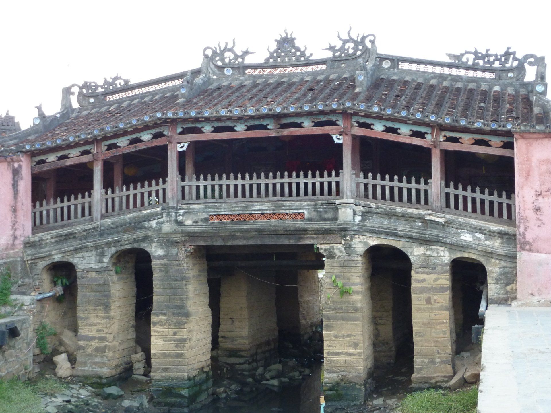Japanse overdekte brug in Hội An, Vietnam, met verweerde stenen steunpilaren en een gedetailleerd houten dak.