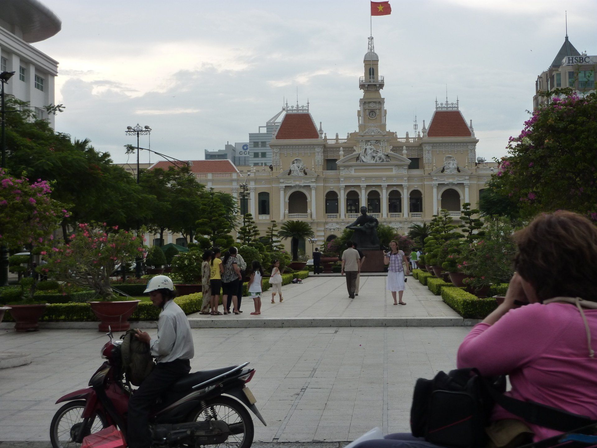 Stadhuis van Ho Chi Minh-stad, Vietnam. Mensen op het plein, motorfiets op de voorgrond, vlag erbovenop.