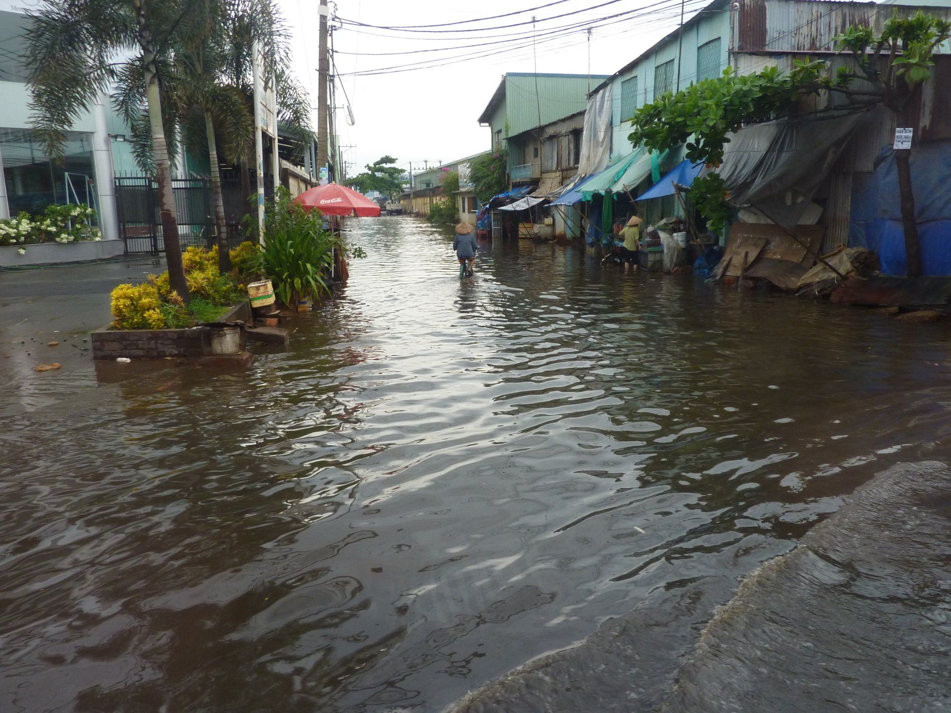 Een ondergelopen straat met winkels en gebouwen. Donker water bedekt de weg en mensen waden erdoorheen.