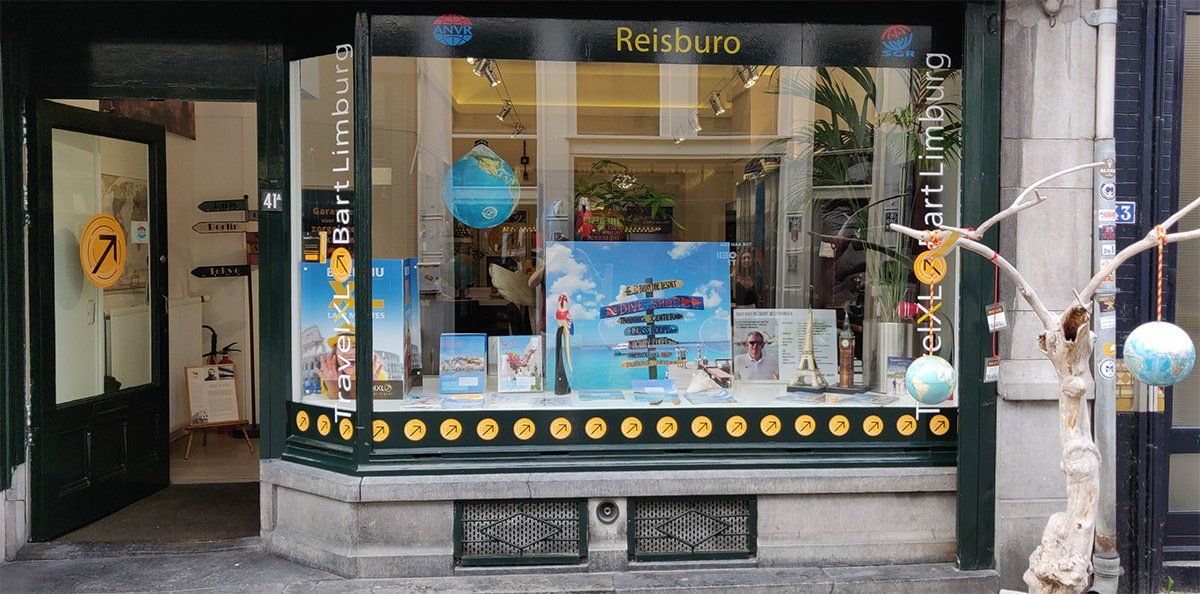 Winkelpui met etalage; reisbureau. Blauw-witte globes en reisaffiches in een stad.