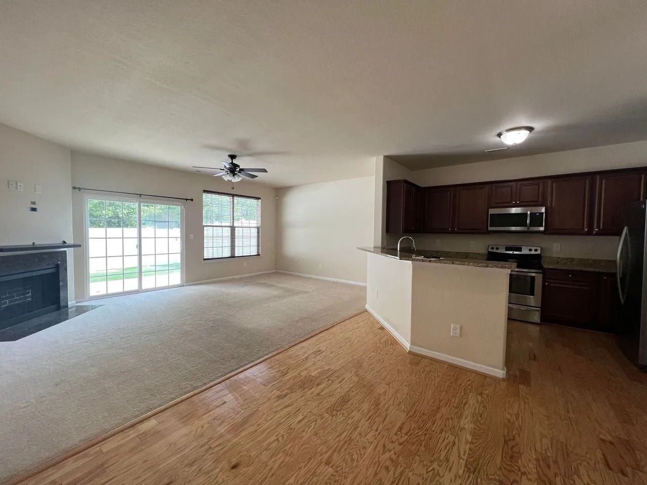 A living room and kitchen in a house with hardwood floors and a fireplace.